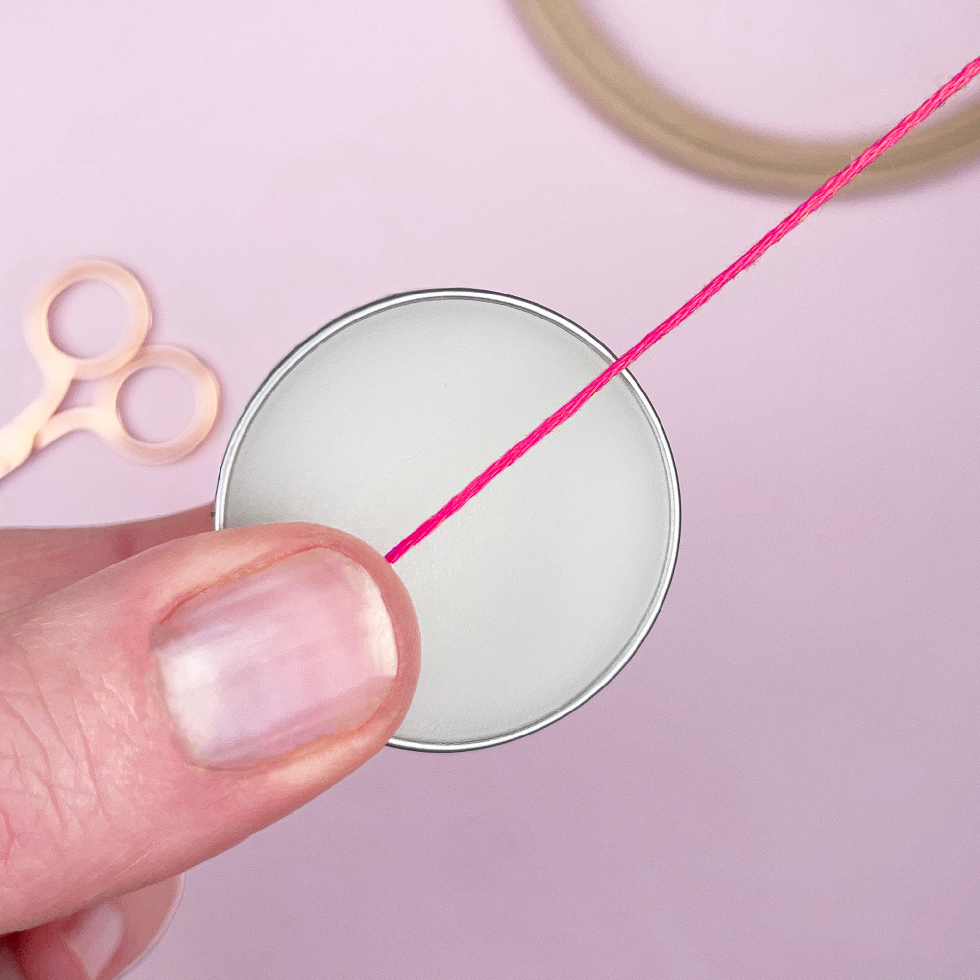 Hand holding pink thread with a spool and scissors on a light pink background