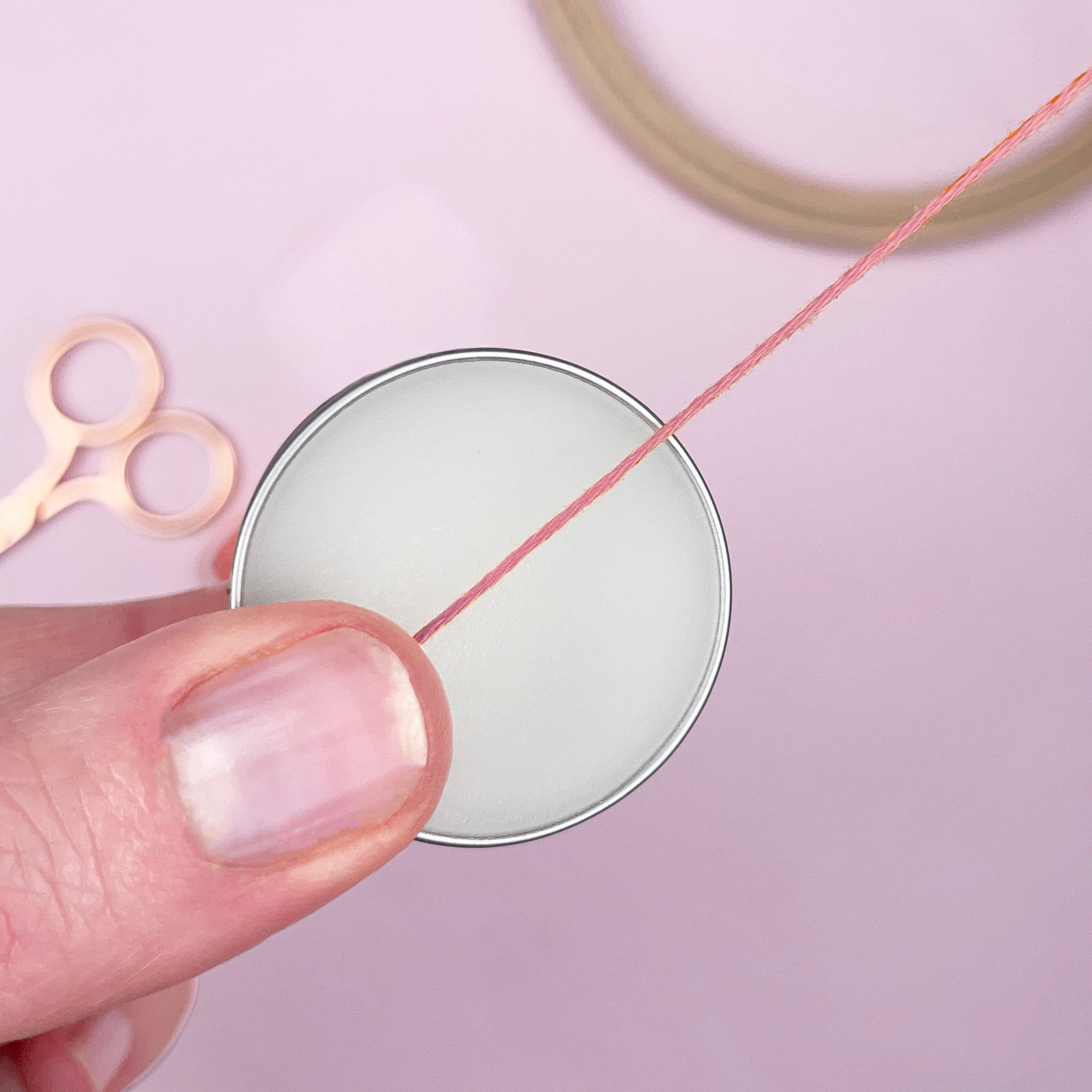 Hand holding a spool of thread with scissors on a pink background