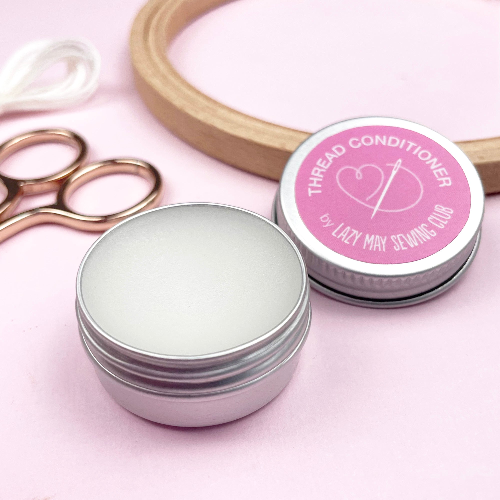 Thread conditioner container with pink lid and scissors on a pink background
