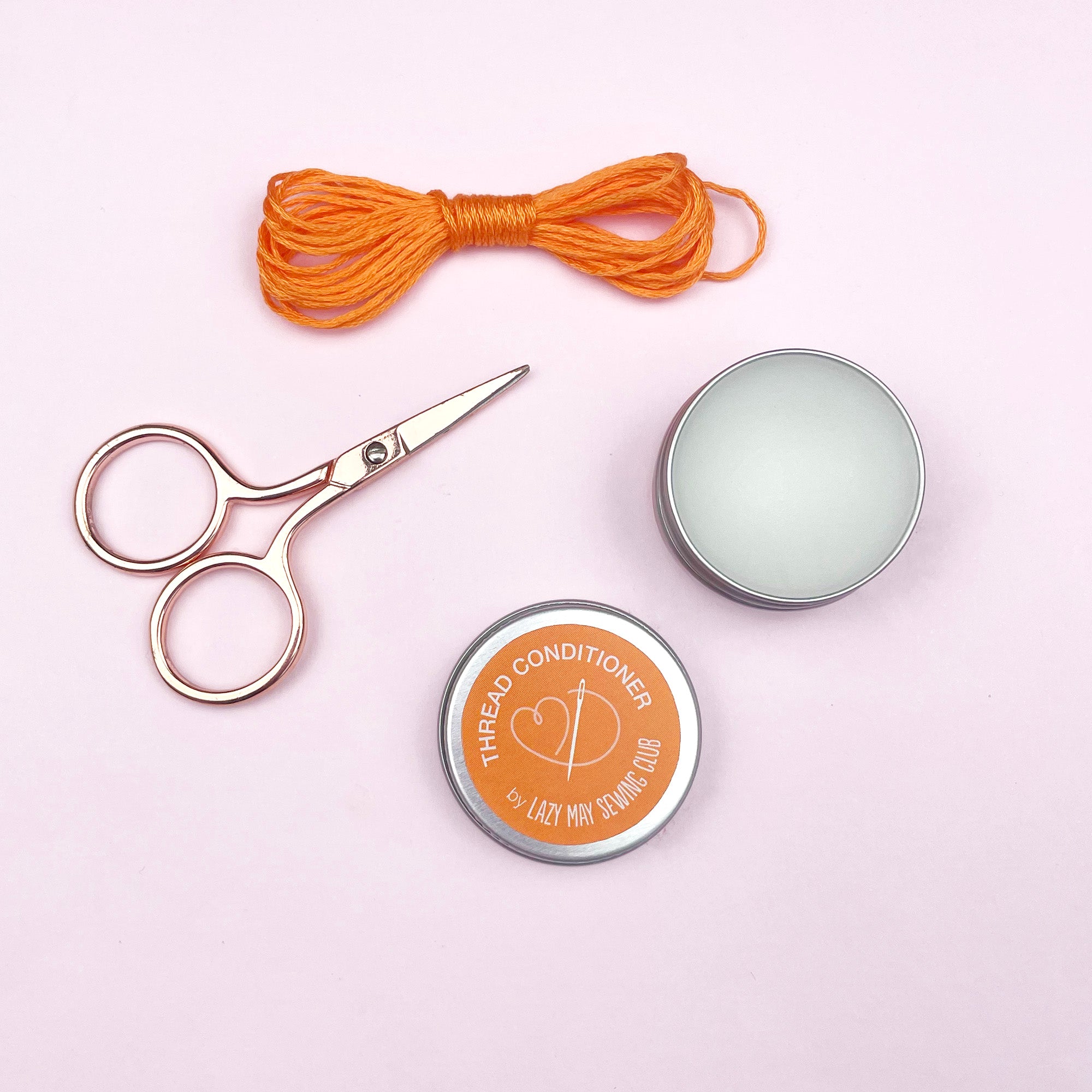 Scissors, thread, and tins labeled 'Thread Conditioner' on a light pink background