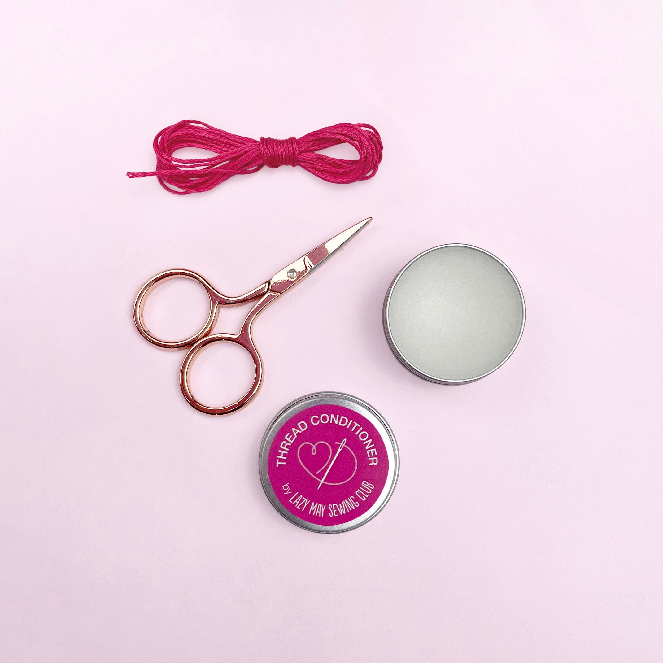 Scissors, thread, and a tin labeled 'Thread Conditioner' on a pink background