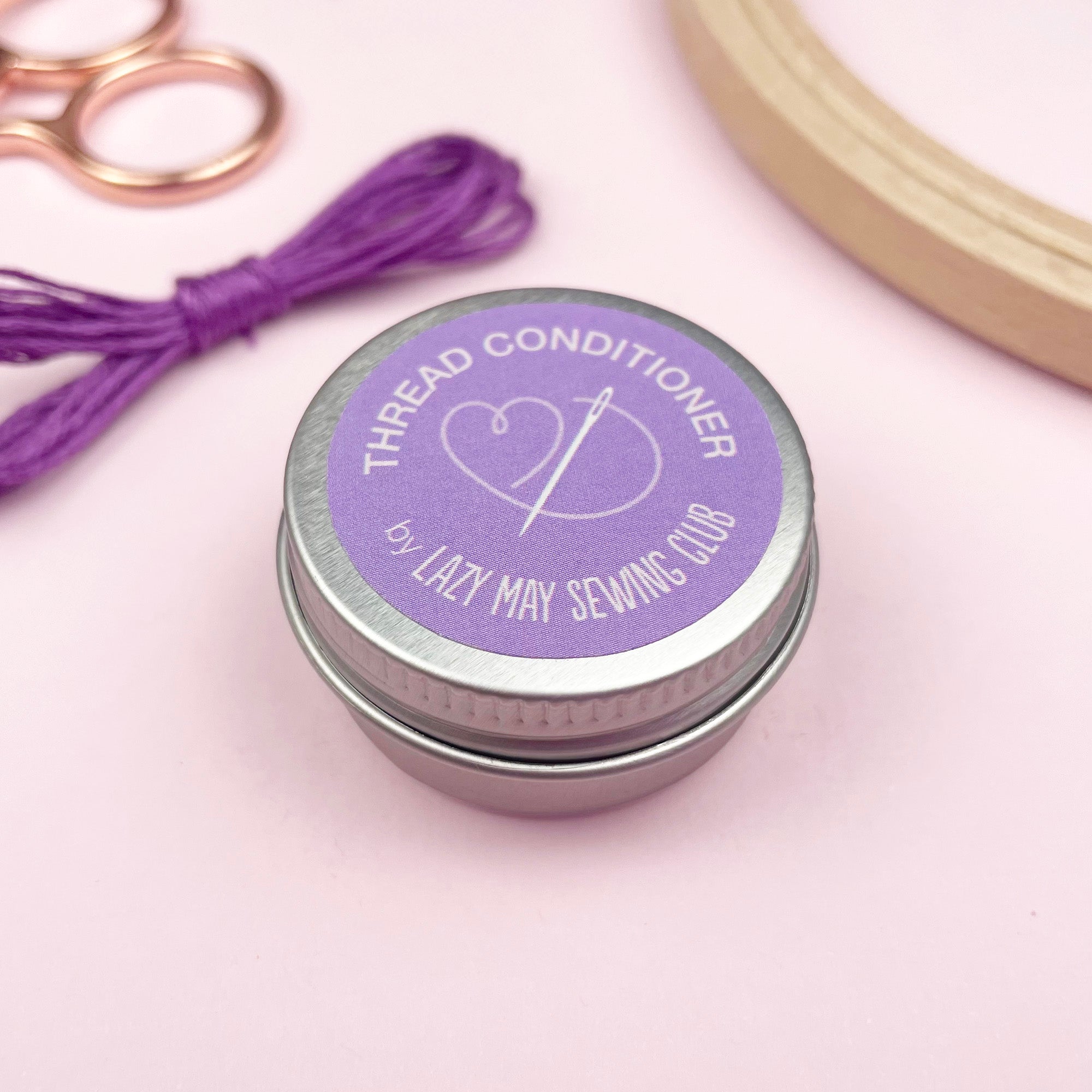 Thread conditioner tin with purple label and thread on a light pink background