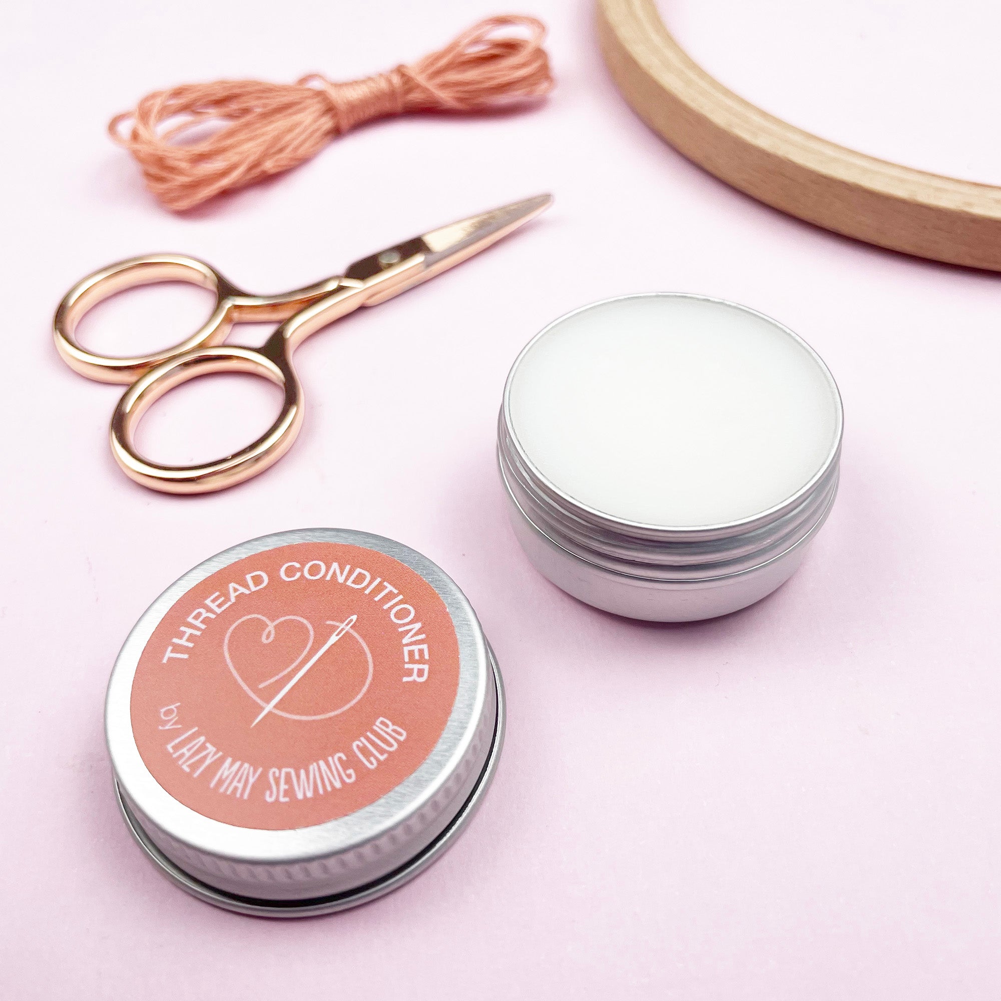 Thread conditioner container with sewing tools on a pink background