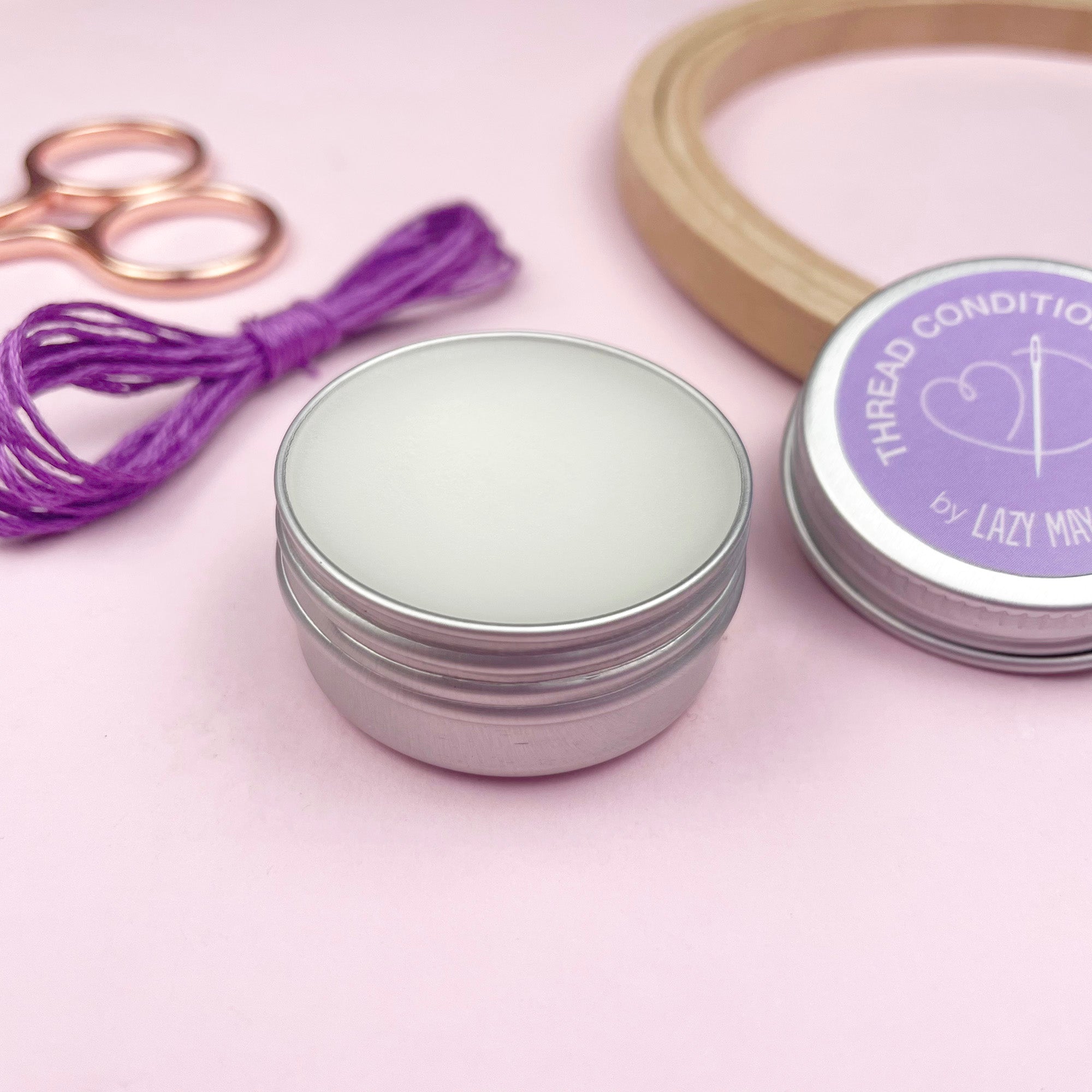 Silver jar with purple lid labeled 'Thread Conditioner by Lazy May' on a pink background.