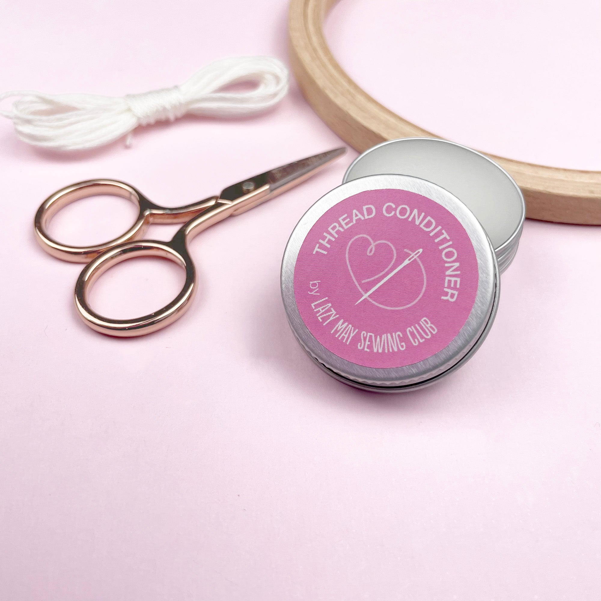 Thread conditioner tin with scissors and thread on a pink background