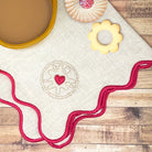 Stick and stitch embroidery pattern of a Jammie Dodger biscuit stitched onto fabric with a scalloped edge, displayed alongside real British biscuits and a cup of tea. A fun and modern embroidery pattern using water-soluble embroidery designs.