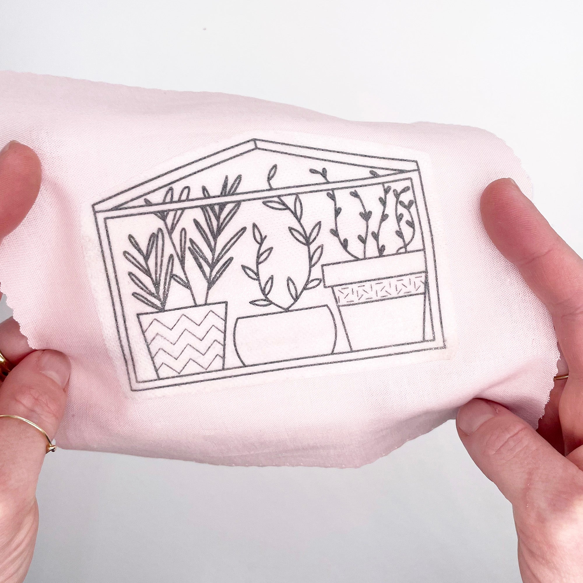 A greenhouse-themed embroidery transfer adhered to pink fabric, ready to be stitched using modern embroidery techniques.