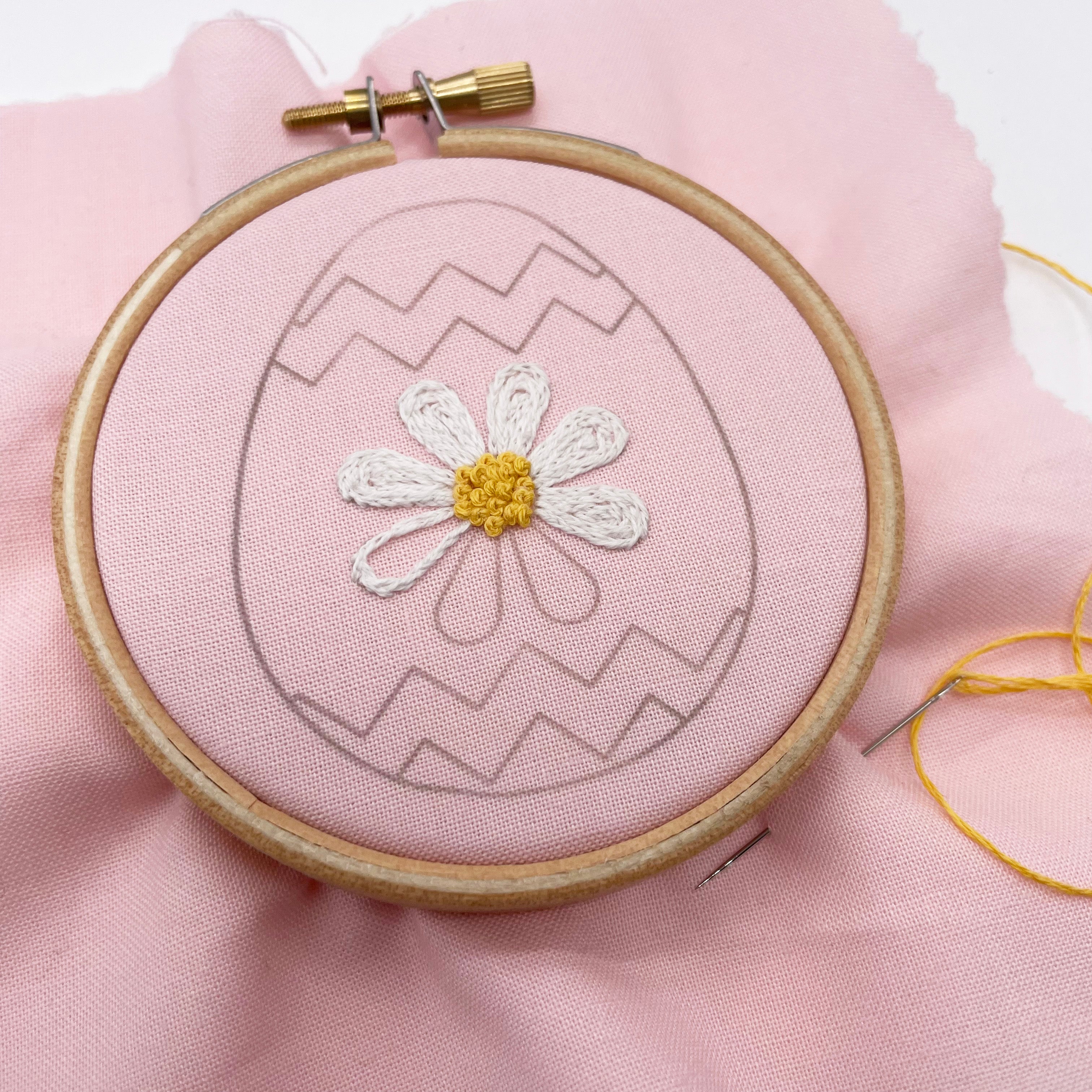 Work-in-progress Easter embroidery pattern featuring a floral Easter egg design transferred onto pink fabric in an embroidery hoop. A great Easter craft for DIY stitchers.