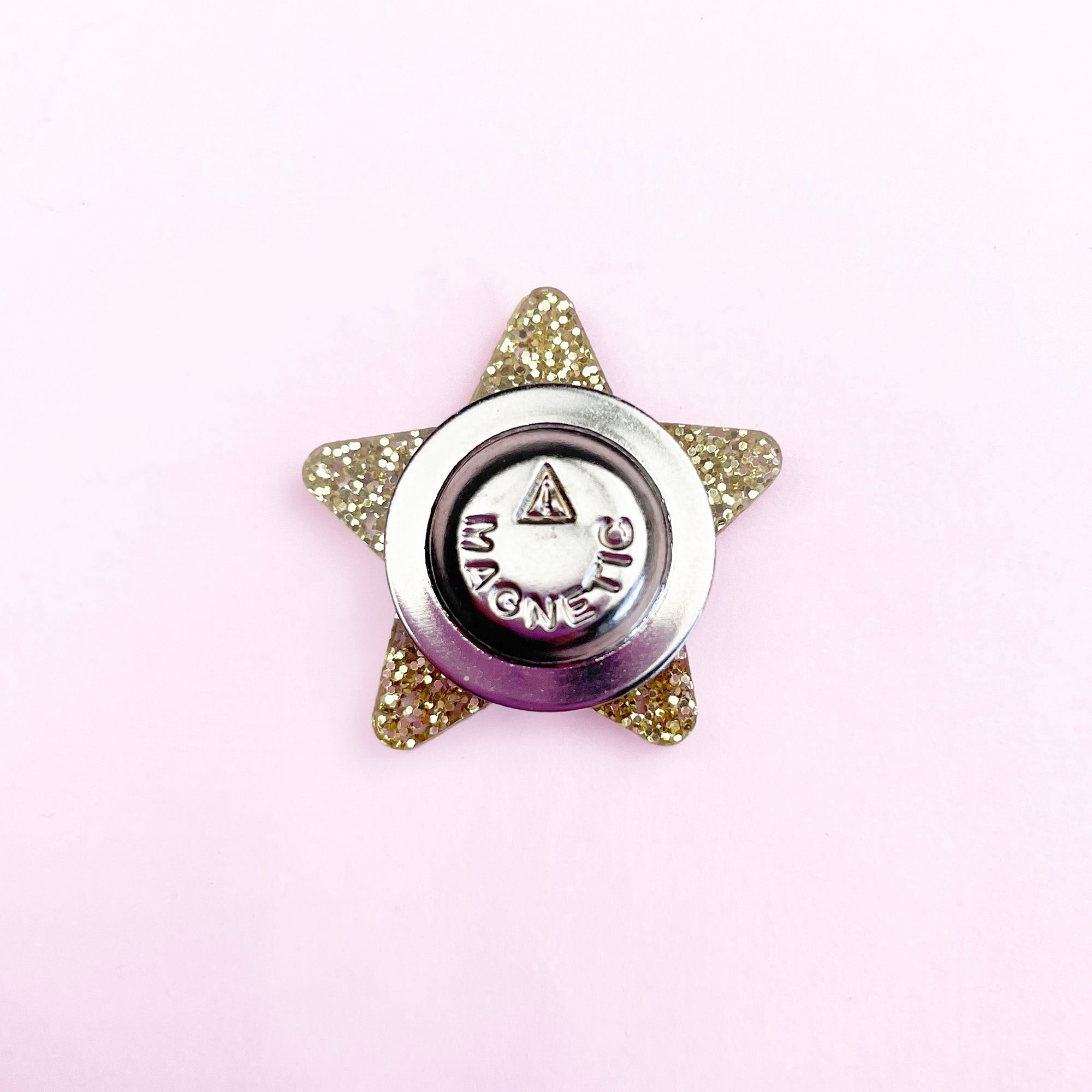 Back view of a gold glitter star magnetic needle minder on a pale pink background