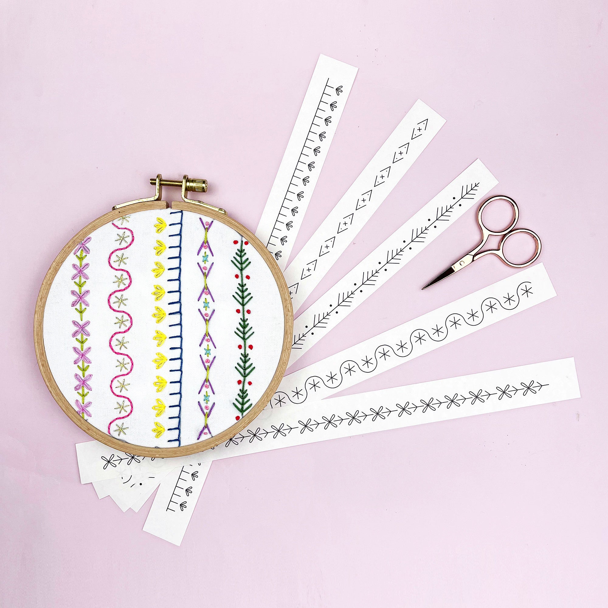Embroidery hoop with pre-printed patterns and scissors on a pink background
