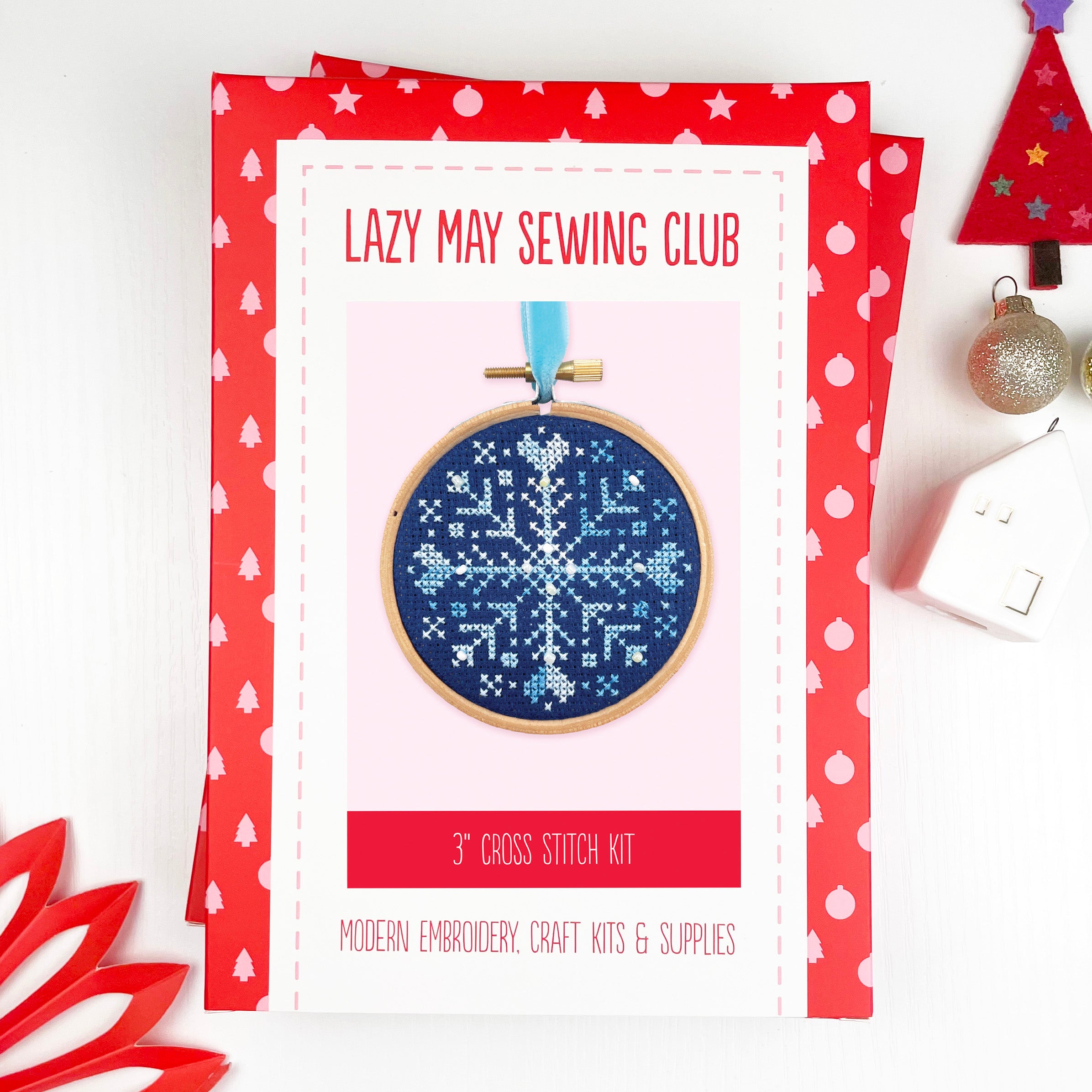 Beaded Snowflake: Christmas Cross Stitch Kit showing a blue and white snowflake embroidery in a wooden hoop with festive decorations nearby