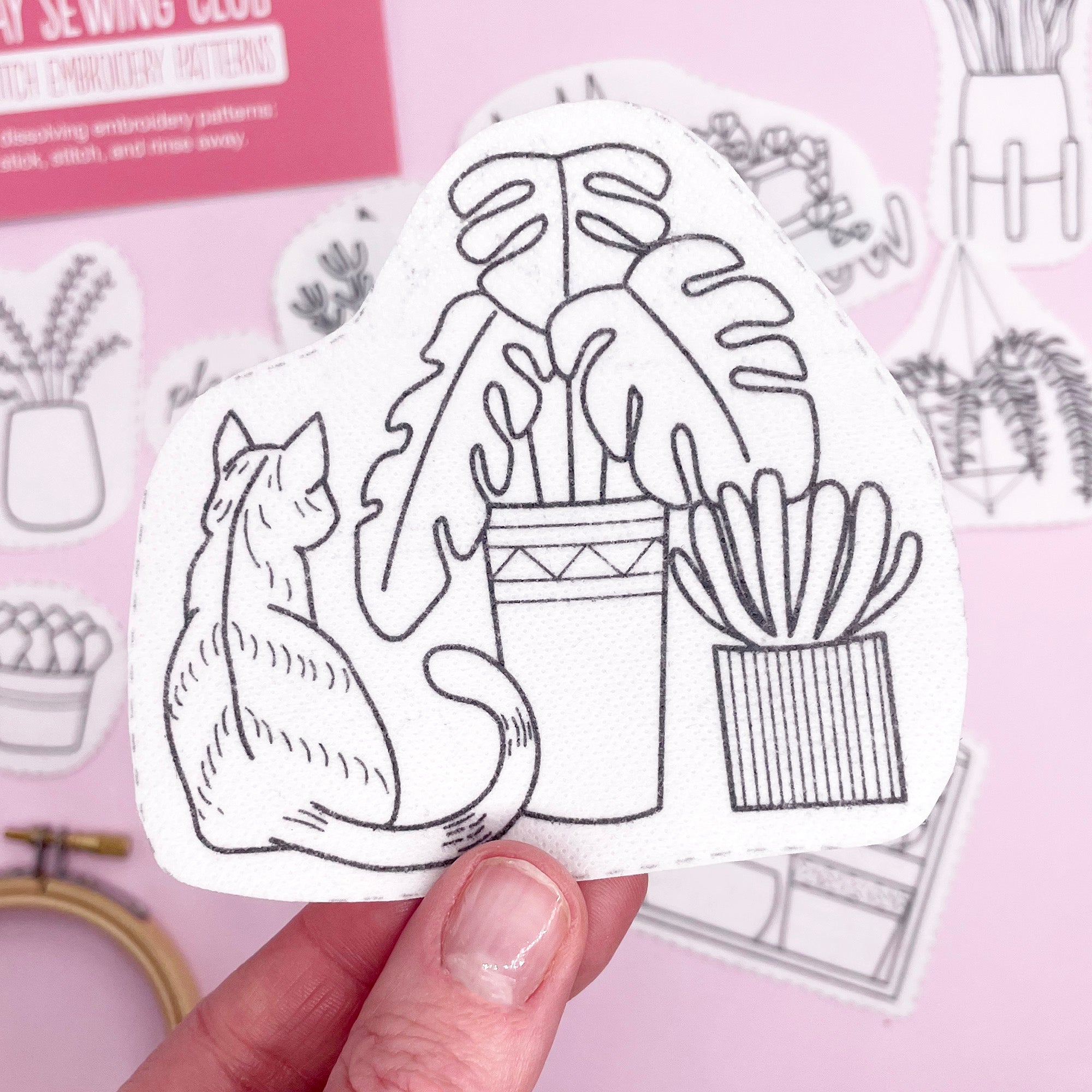 A close-up of a dissolving embroidery transfer featuring a botanical scene with a cat, ready to be stitched onto fabric.