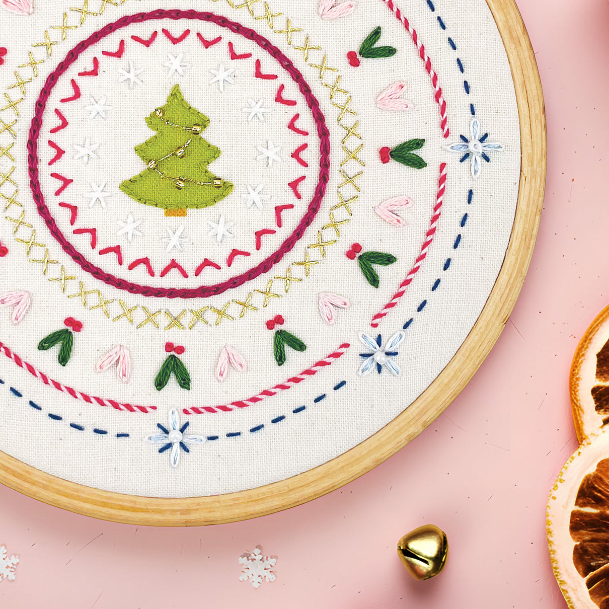 Embroidery hoop with Christmas-themed stitching on a pink background