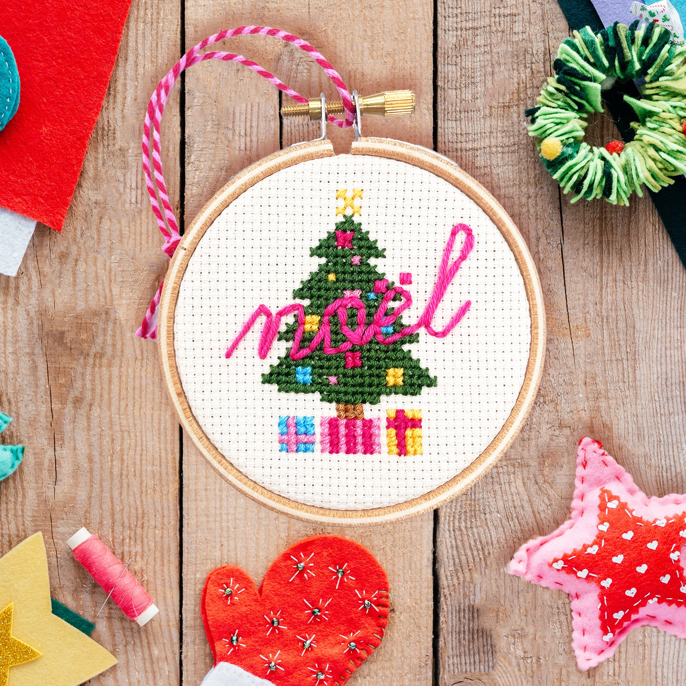 Christmas Tree: Cross Stitch Kit featuring a stitched Christmas tree with gifts and the word noel in pink thread