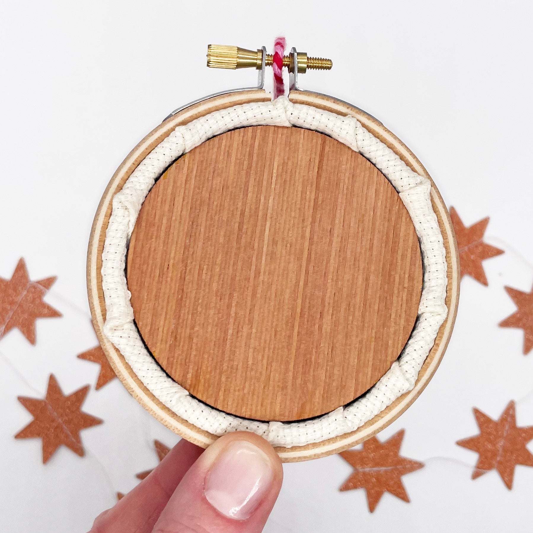 Wooden backing and fabric in an embroidery hoop for the Christmas Tree: Cross Stitch Kit with star decorations in background