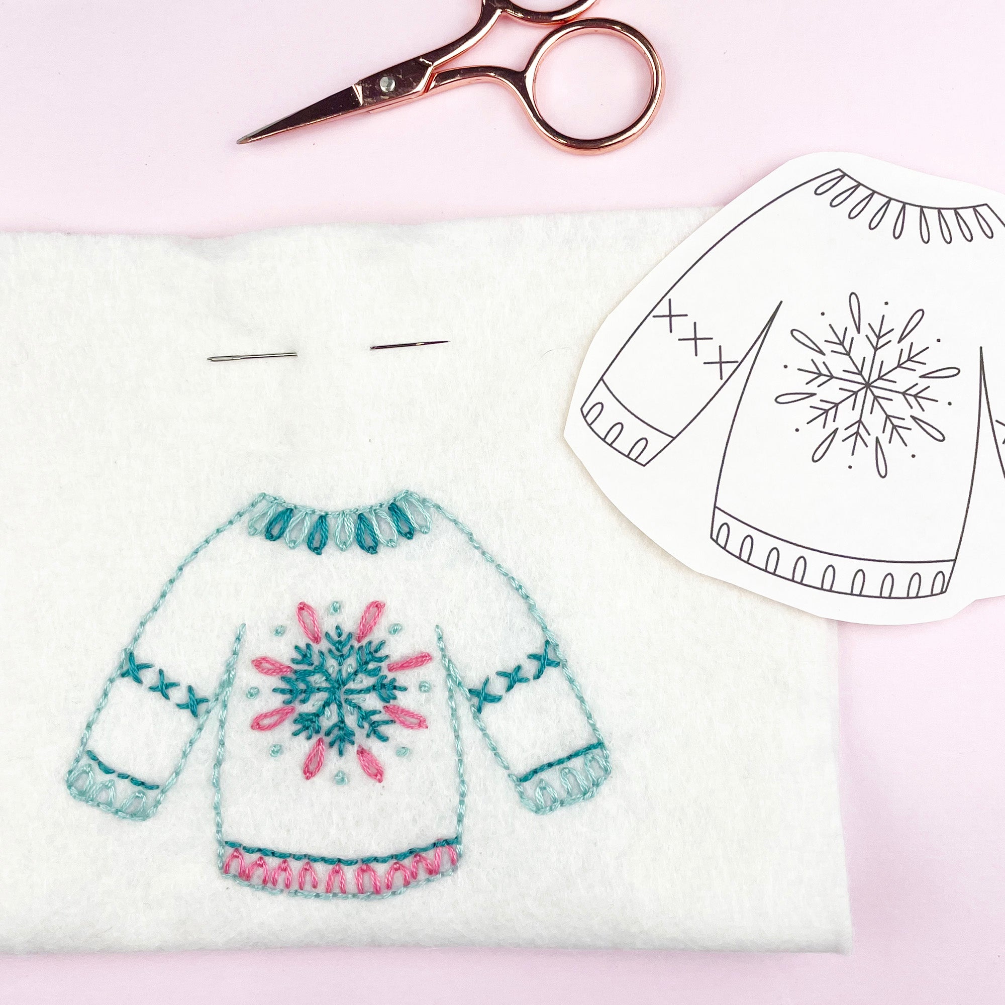 Embroidery project with a sweater design, scissors, and pattern on a light pink background