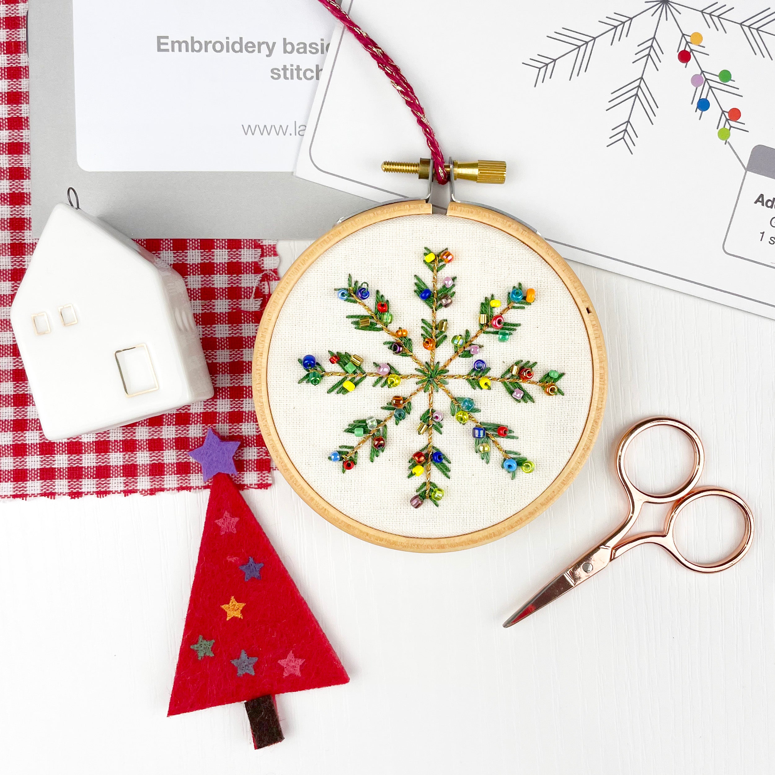Embroidery hoop with a colorful snowflake design on a white surface with sewing tools.