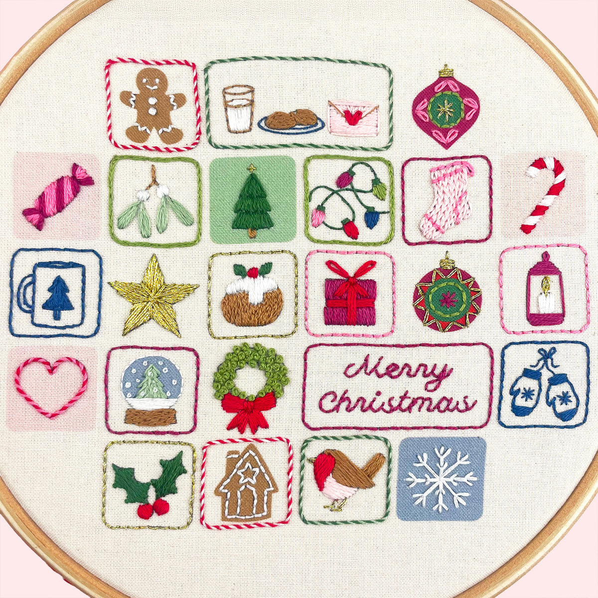A circular embroidery advent calendar hoop containing a festive Embroidery advent calendar design with multiple small holiday motifs, including gingerbread men, Christmas trees, stockings, candy canes, ornaments, a wreath, and the words “Merry Christmas,” stitched on light pink fabric.