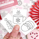 Hand holding a card with black line art designs of a cup, snowflake, and penguin on a pink background.
