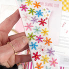 Hand holding a white fabric bookmark with colorful embroidered flowers, with 'May Sewing Club' in the background.