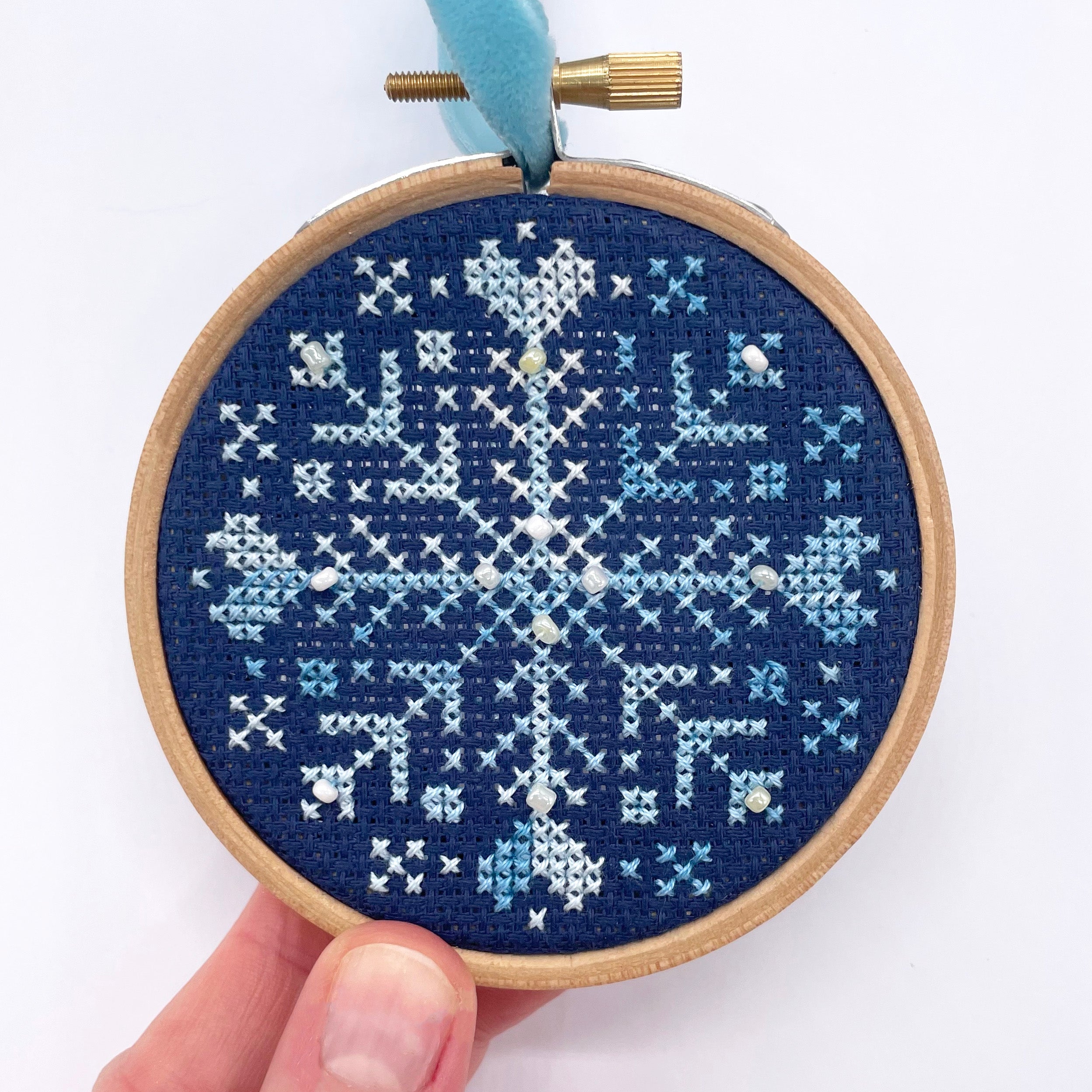 Beaded Snowflake: Christmas Cross Stitch Kit featuring a blue and white snowflake with beads on dark fabric in a wooden hoop