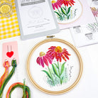 Embroidery hoop with floral coneflower design on a table with embroidery threads and patterns.