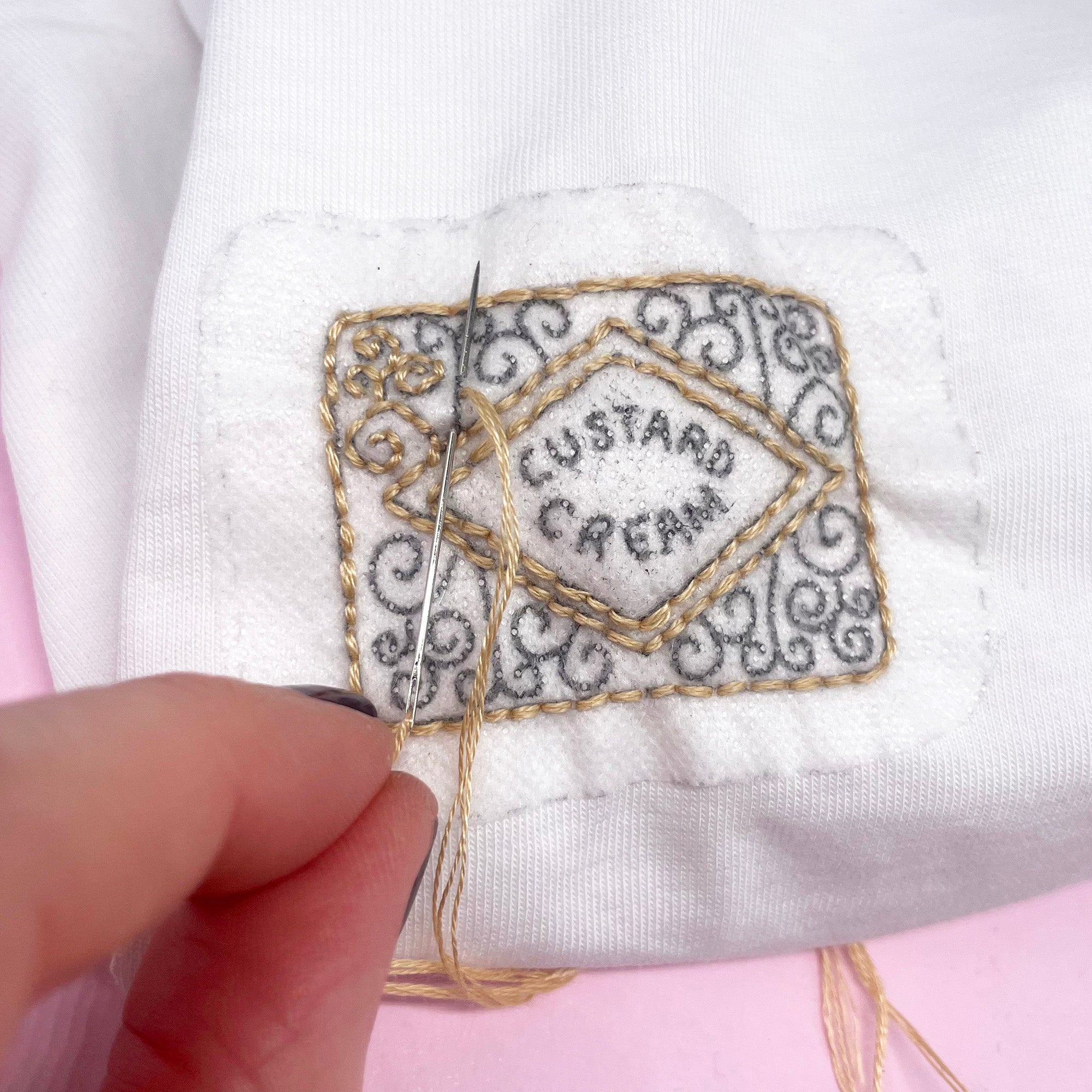 In-progress embroidery of a custard cream biscuit design using a stick and stitch embroidery pattern on white fabric. This water-soluble embroidery pattern dissolves after stitching for a seamless look.