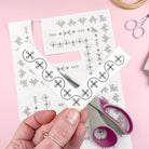 A hand holding one of the corner Stick & Stitch designs, scissors and napkin in the background.
