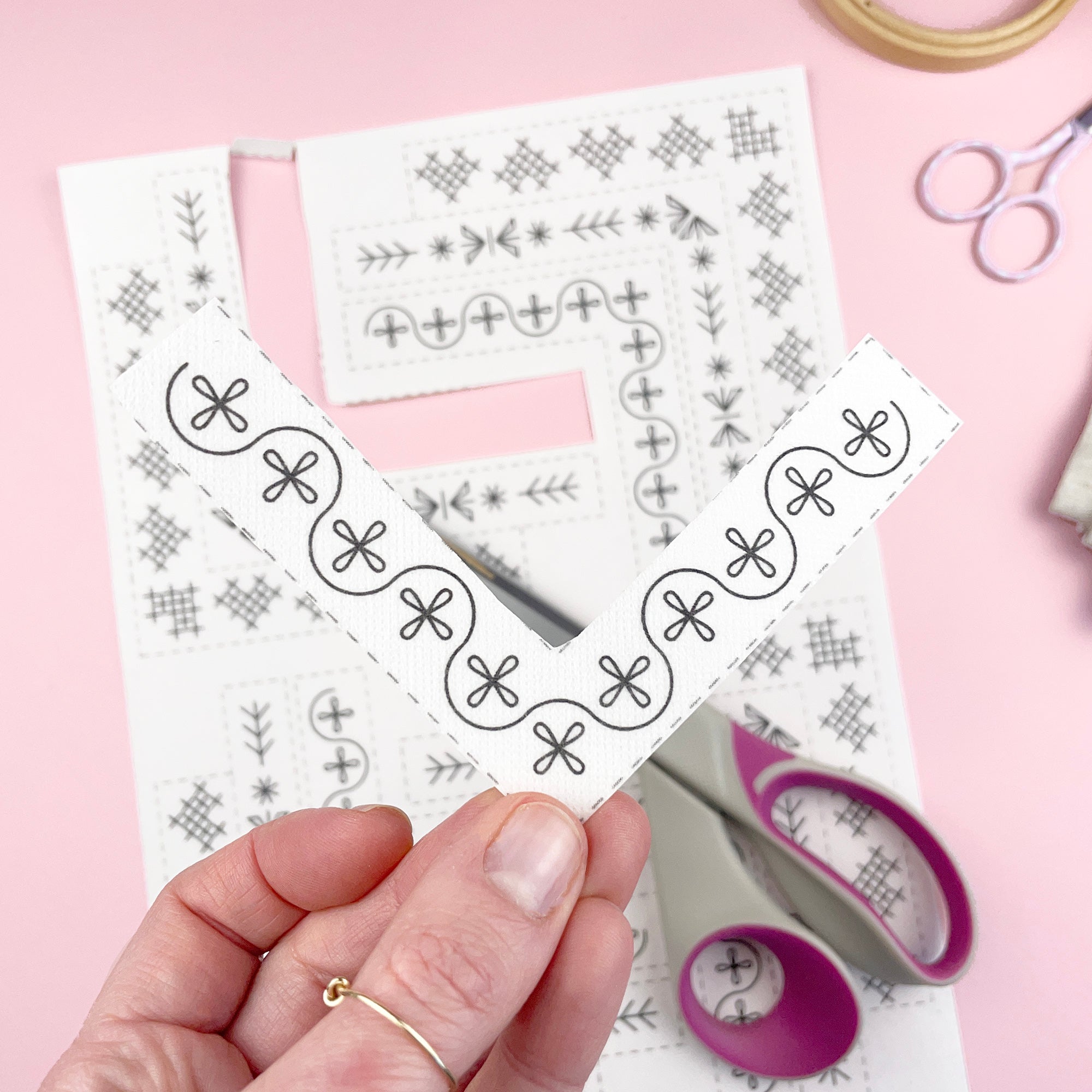 A hand holding one of the corner Stick & Stitch designs, scissors and napkin in the background.