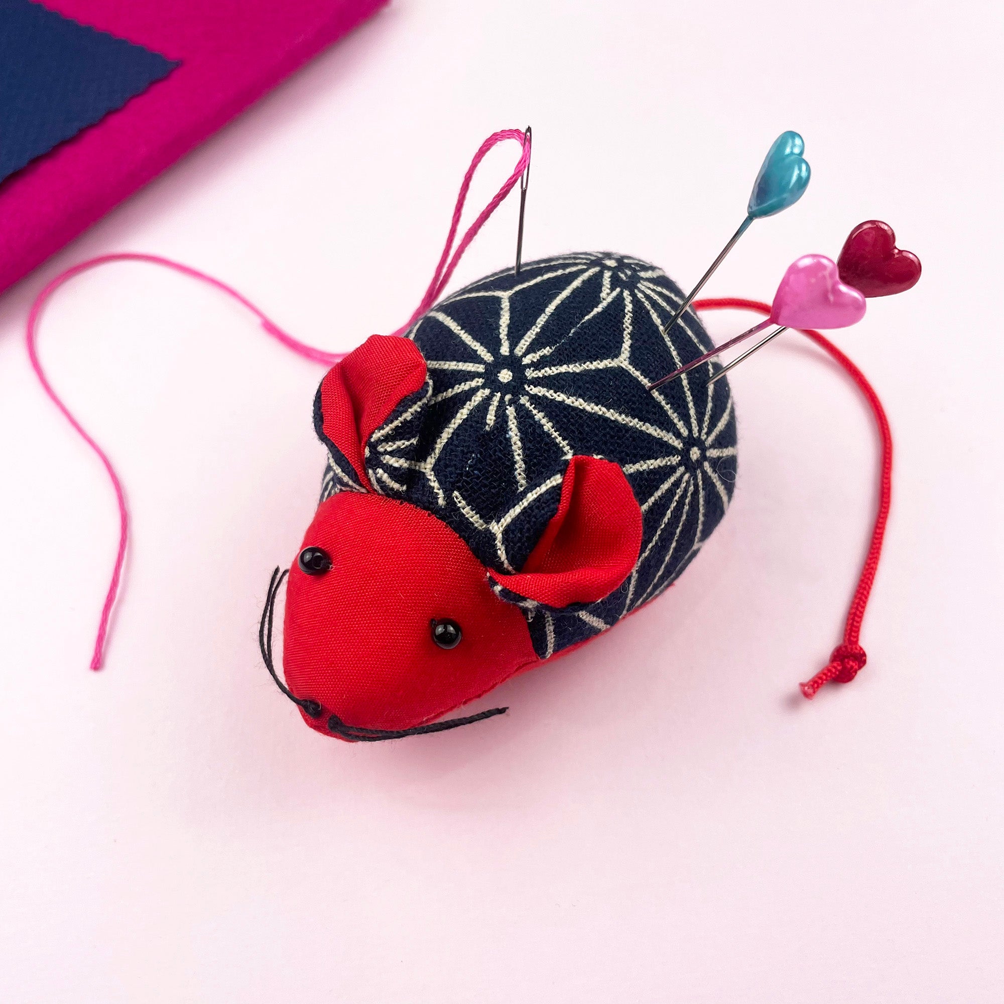 Cute red and navy mouse pin cushion made from cotton, holding sewing pins with heart-shaped heads.