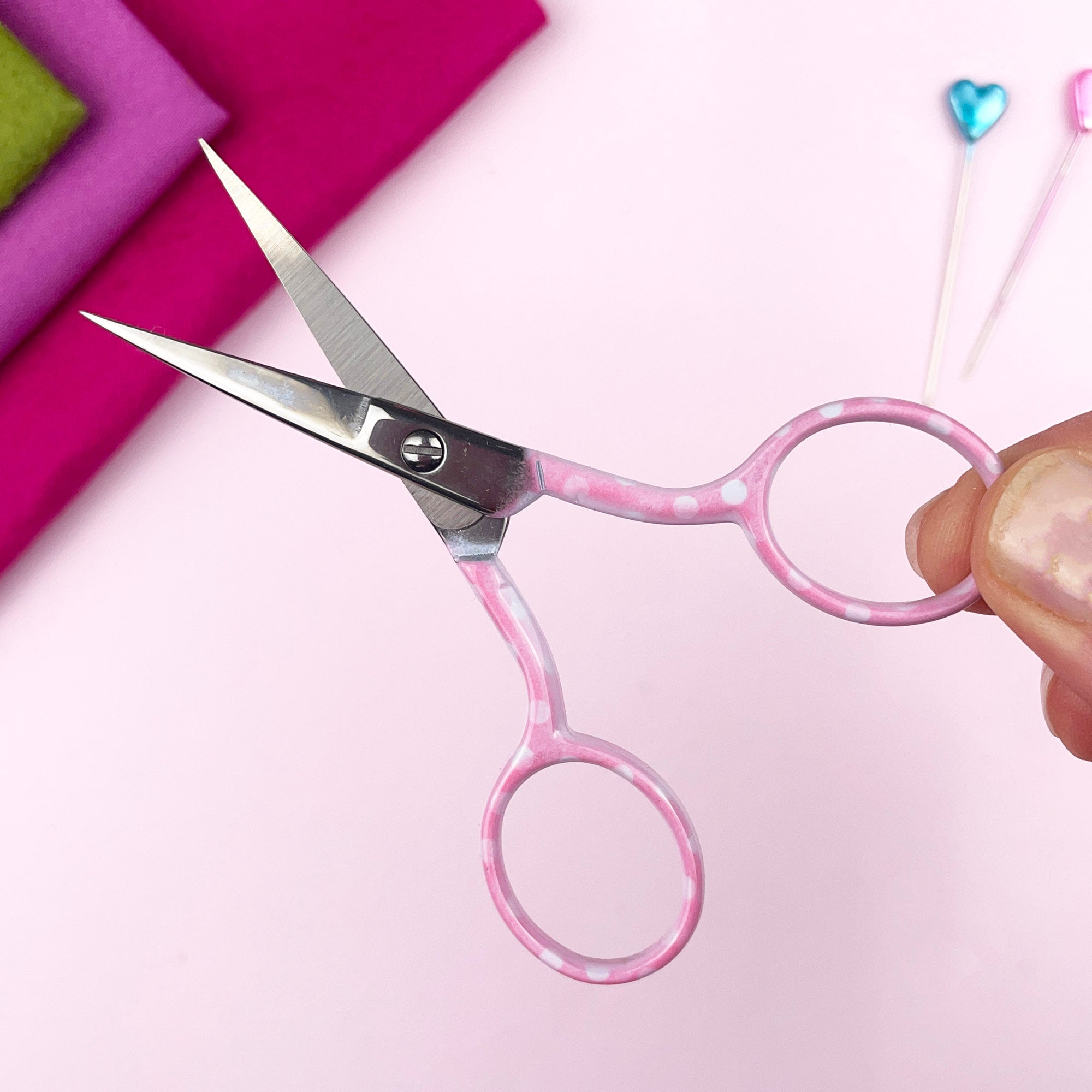 Pink-handled scissors held by a hand on a pink background