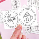 Hand holding a card with black embroidery pattern designs on a pink background