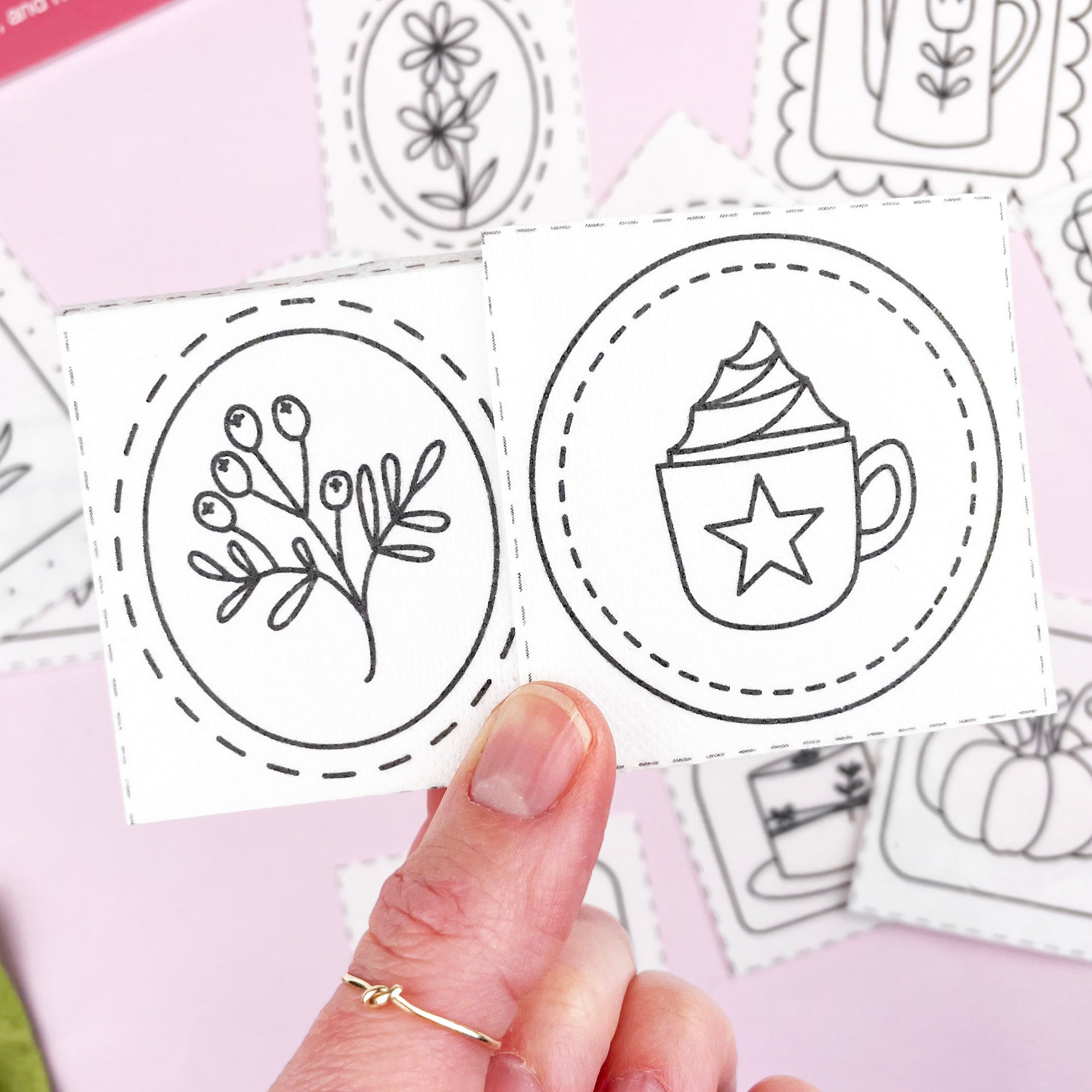 Hand holding a card with black embroidery pattern designs on a pink background