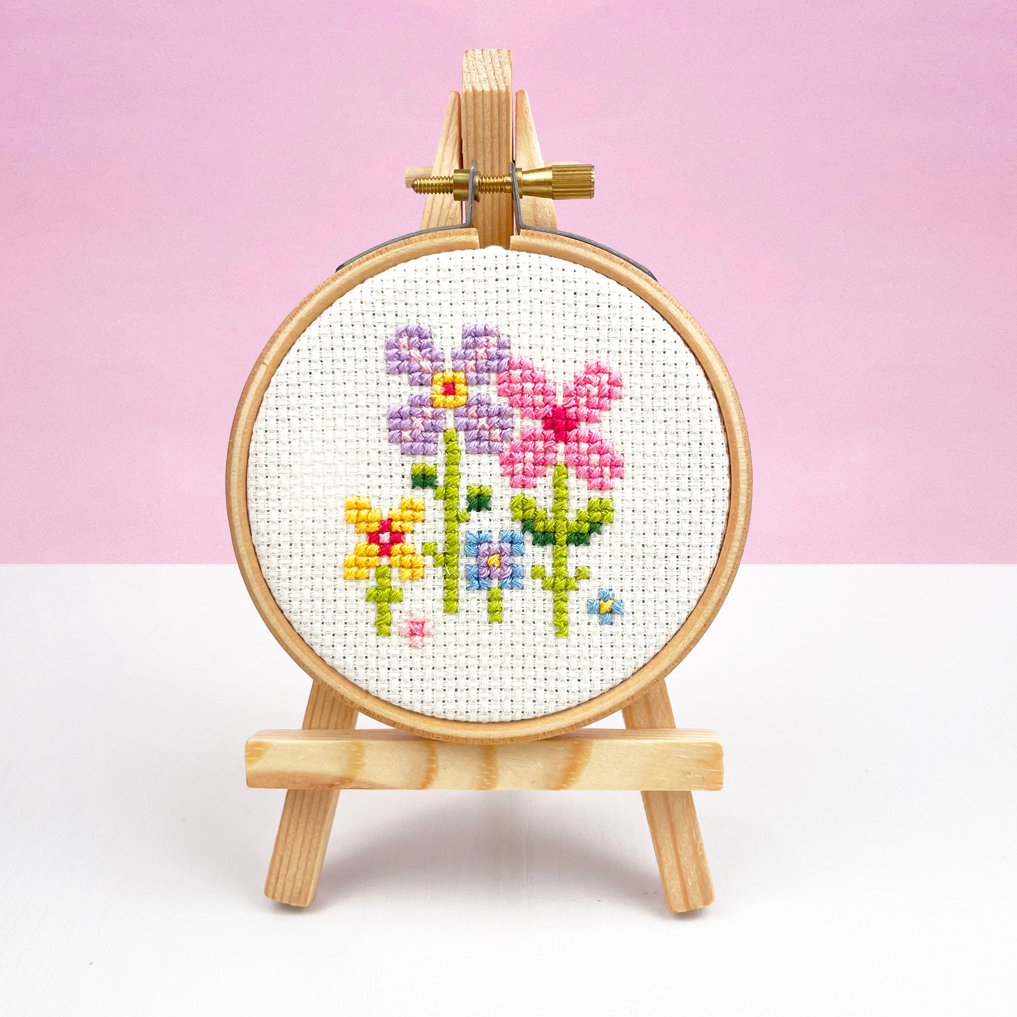 Small Wooden Easel: Embroidery Hoop Display Stand holding a colorful floral cross stitch embroidery on white fabric.