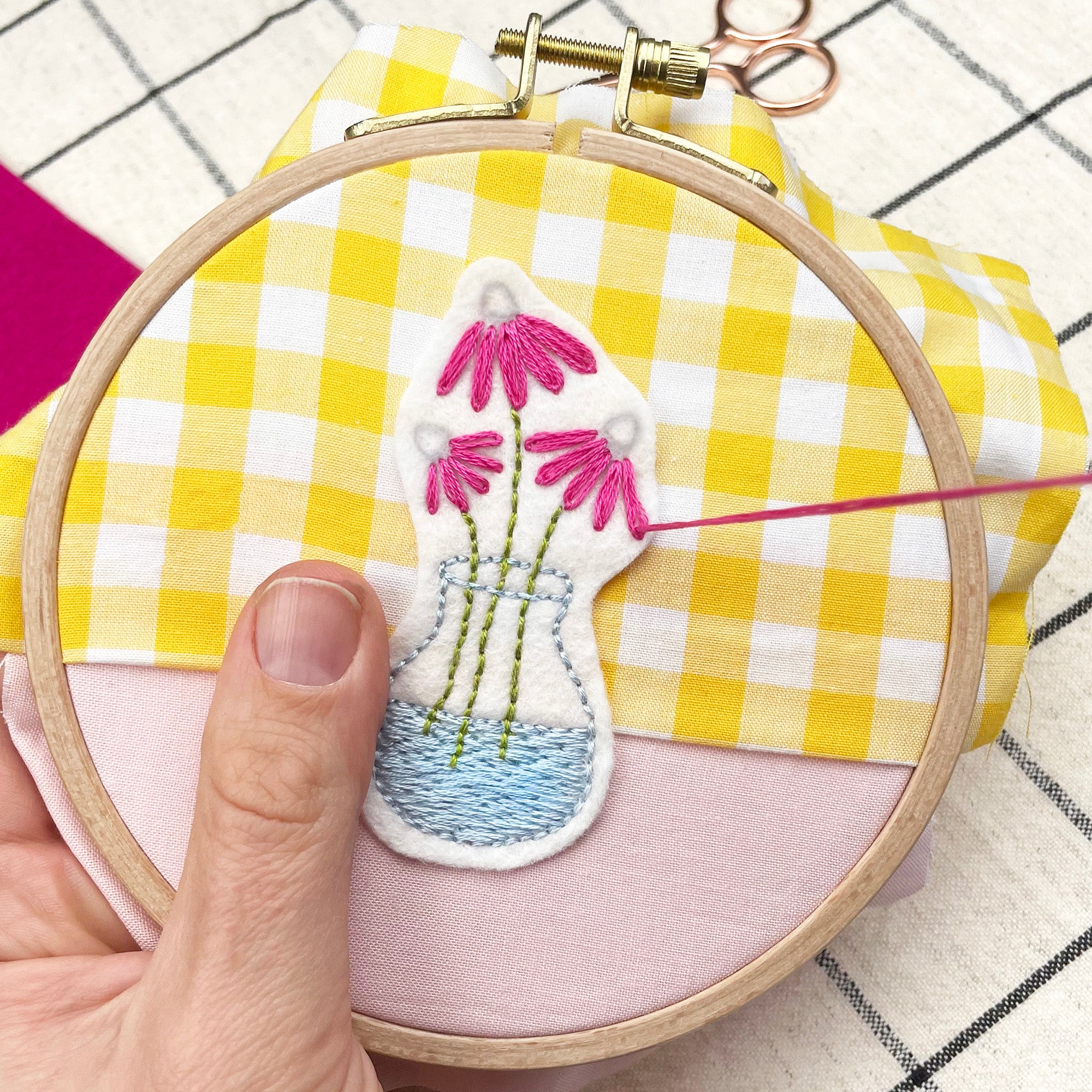 hands embroidering a hoop with a flower vase design