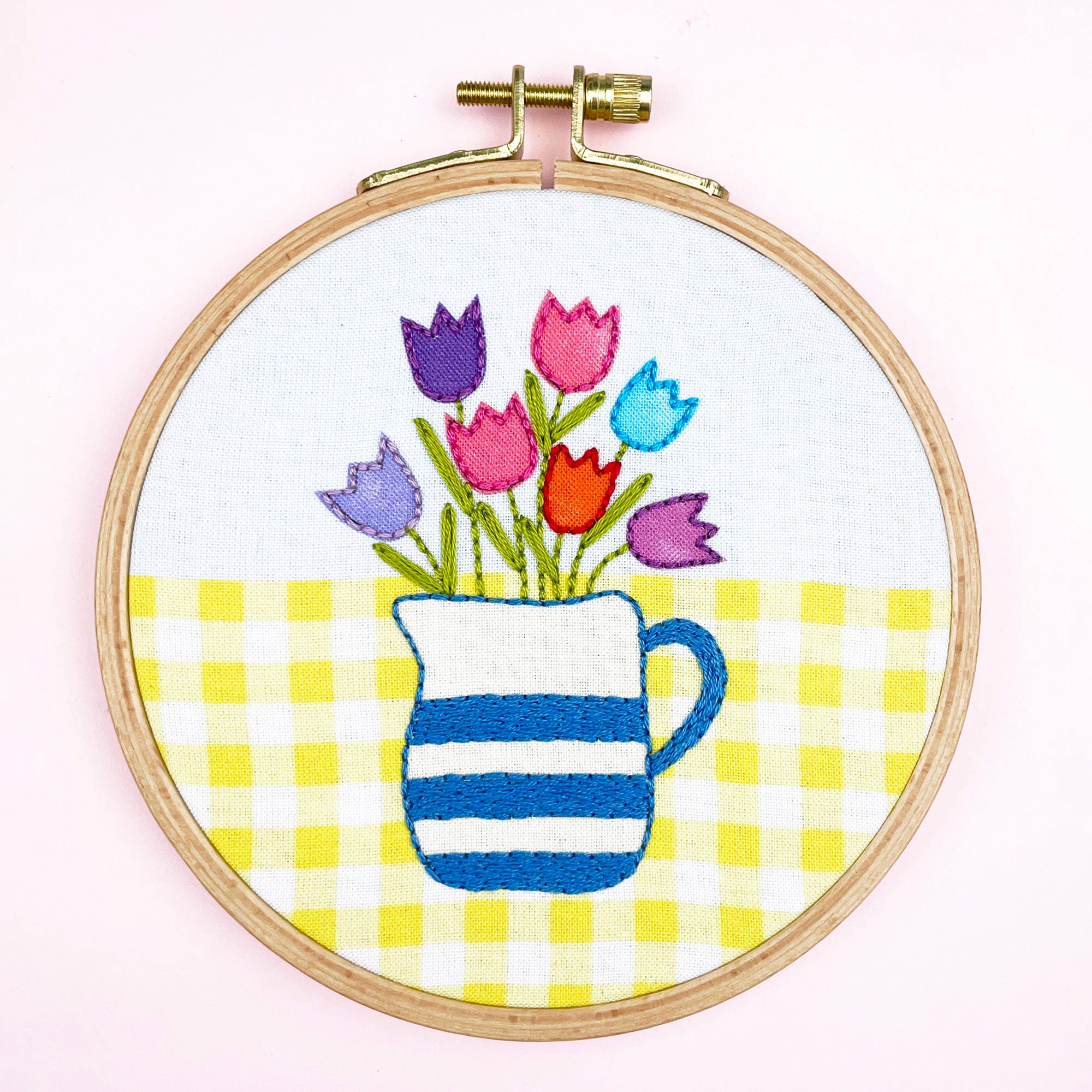 Embroidery hoop with colorful tulips and a striped pitcher on a yellow and white checkered background.