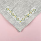 Yellow floral embroidery stitched in a corner design on the edge of a grey linen napkin.