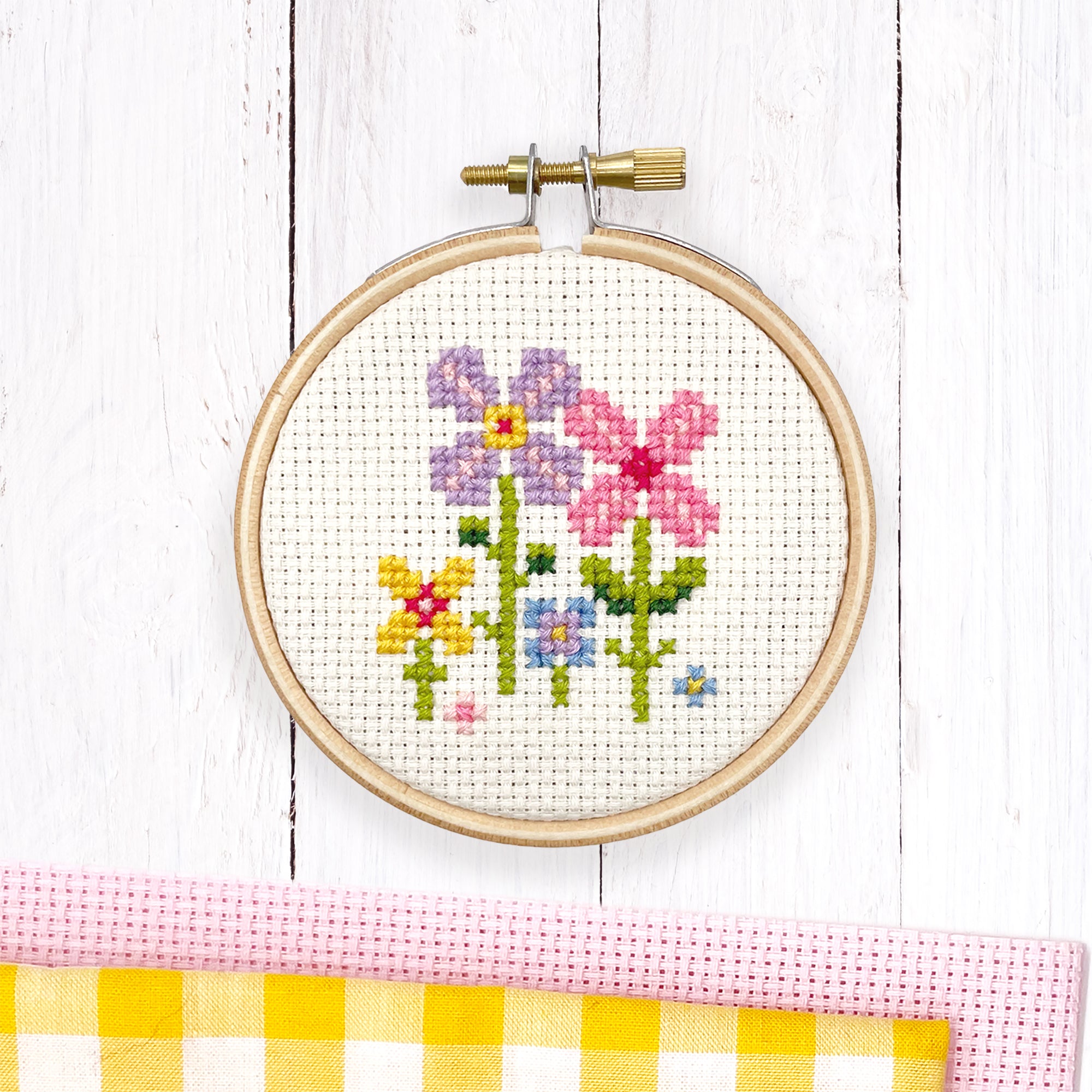 Tiny Garden: Cross Stitch Kit showing colorful floral embroidery in wooden hoop on white wood background