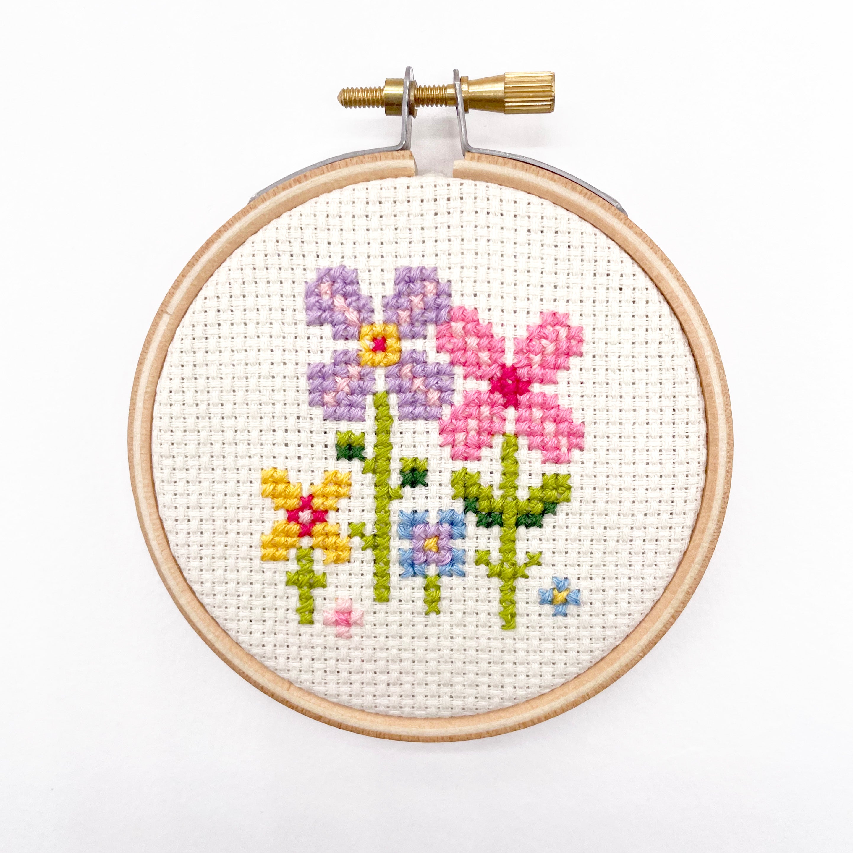 Tiny Garden: Cross Stitch Kit with colorful floral embroidery in a wooden hoop on white fabric background
