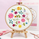 Finished wildflower embroidery hoop on wooden stand, part of a DIY floral hand embroidery kit for adults.
