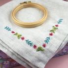 Colourful floral corner embroidery stitched on a grey cushion cover with embroidery hoop.