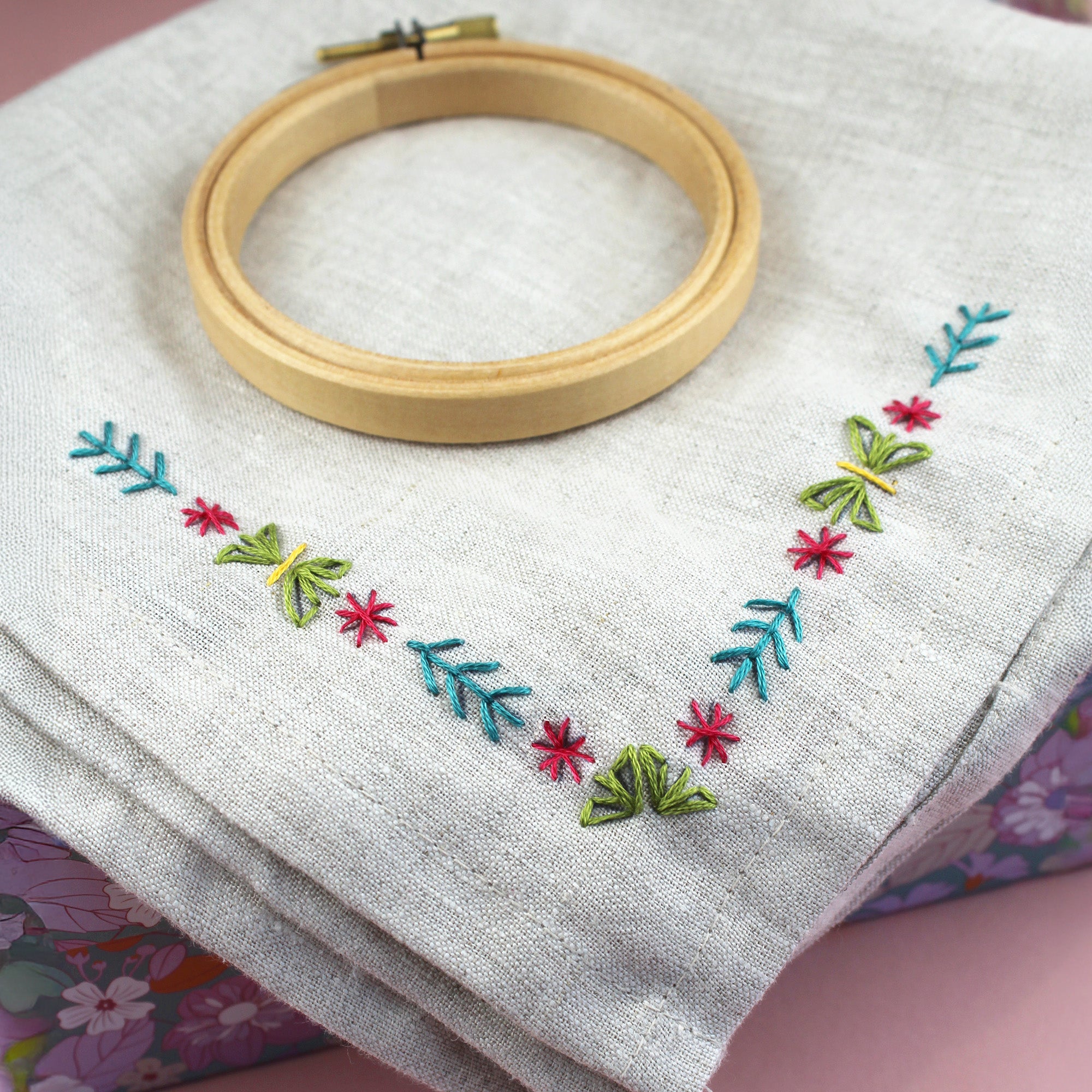 Colourful floral corner embroidery stitched on a grey cushion cover with embroidery hoop.
