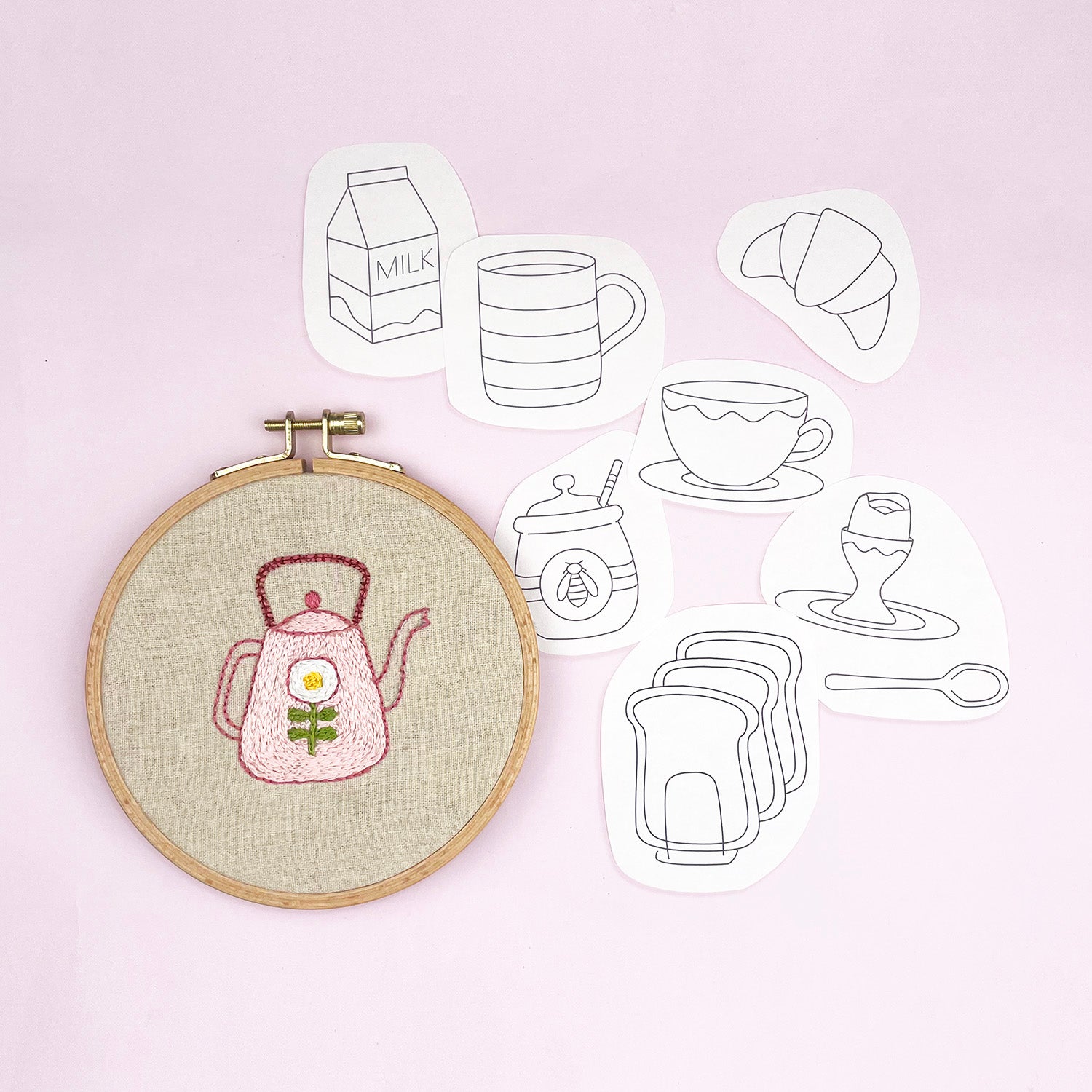 Embroidery hoop with a pink teapot design on a light background with tea-themed embroidery transfers.