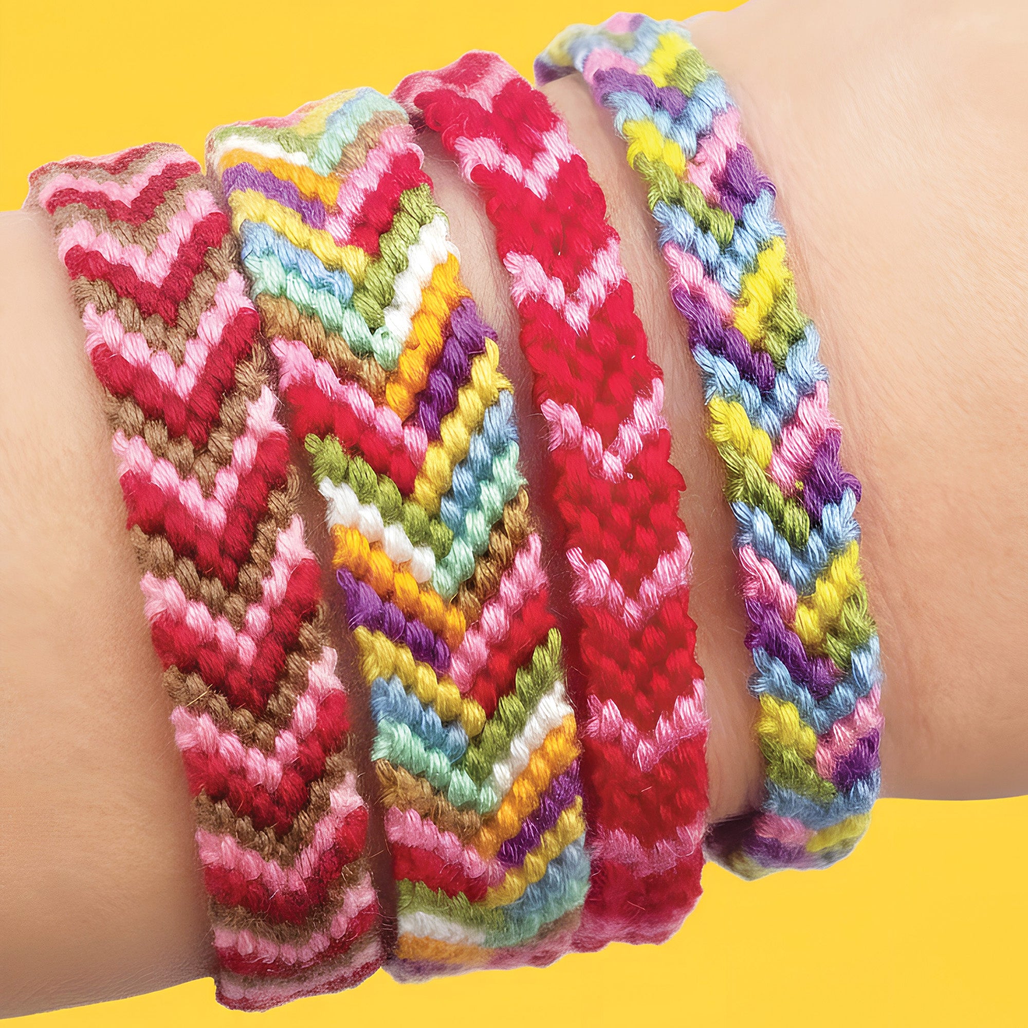 Colorful braided bracelets on a wrist against a yellow background, made from a friendship bracelet making kit. traditional knotted bracelets