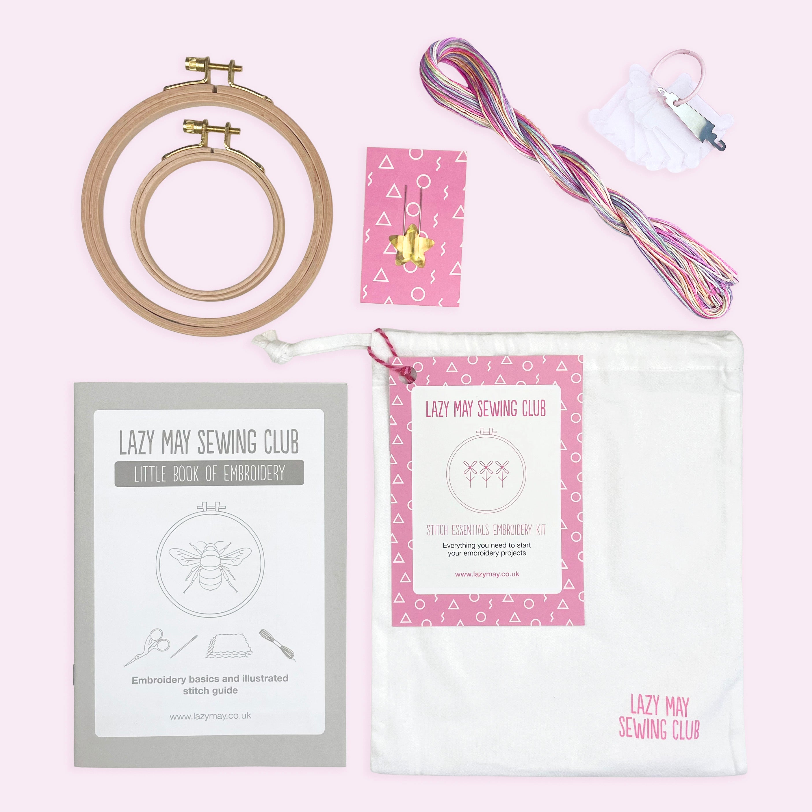 Embroidery kit with wooden hoops, pastel multicolor threads, stitch guide, needle set, and storage bag on pink background