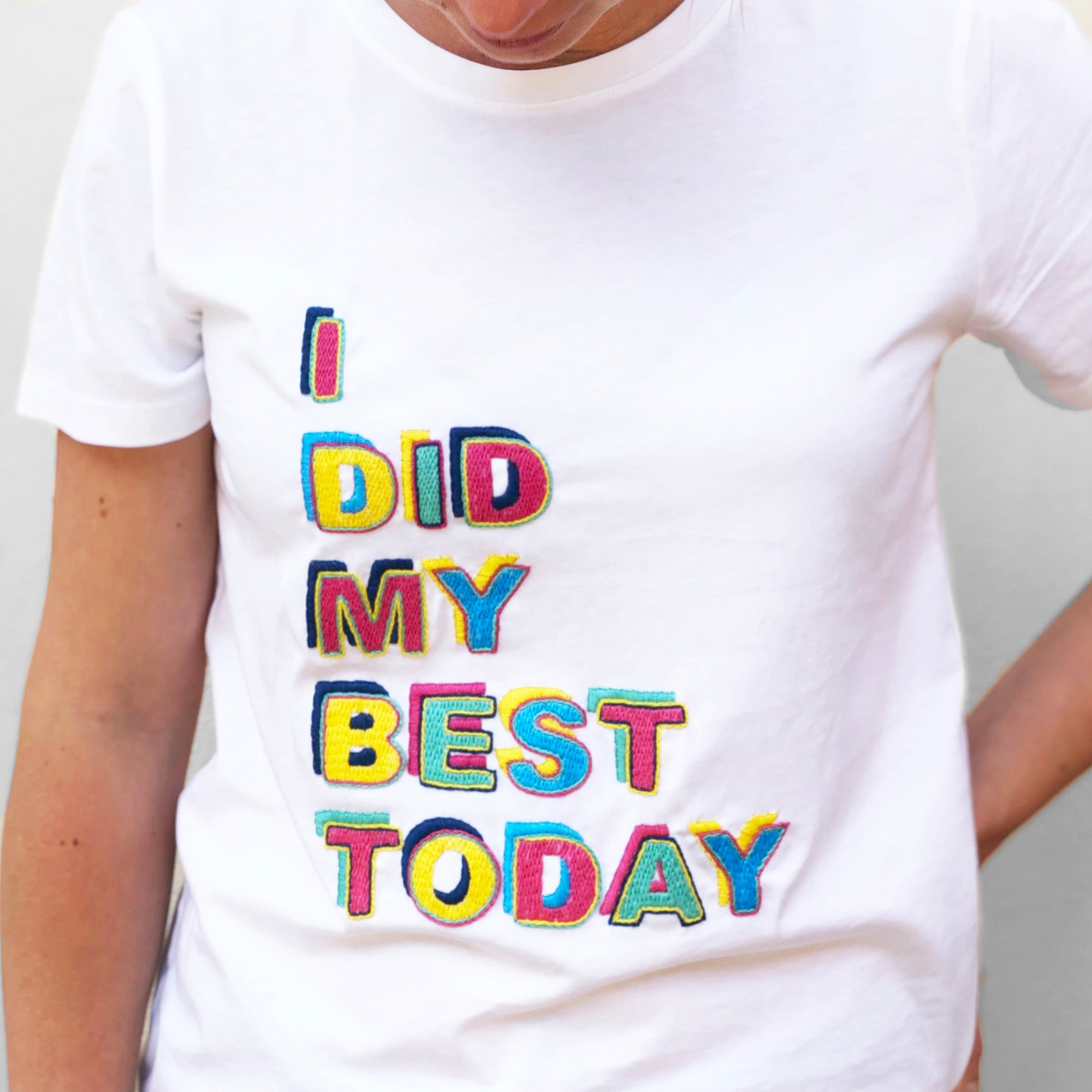 Person wearing a white shirt with colorful embroidered letters made using Iron-On Embroidery Patterns: 26 Bold Alphabet Letter Designs