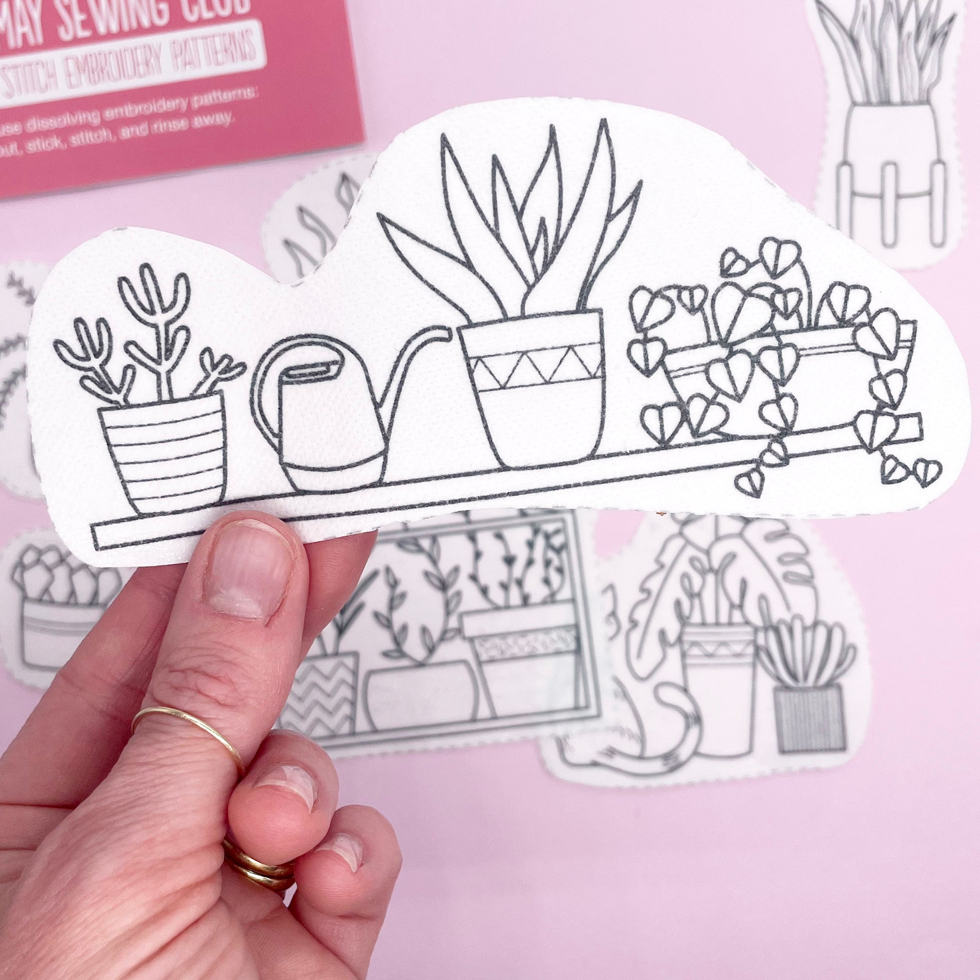 A dissolving embroidery pattern with an illustrated shelf of potted plants and a watering can, designed for easy stick and stitch embroidery.