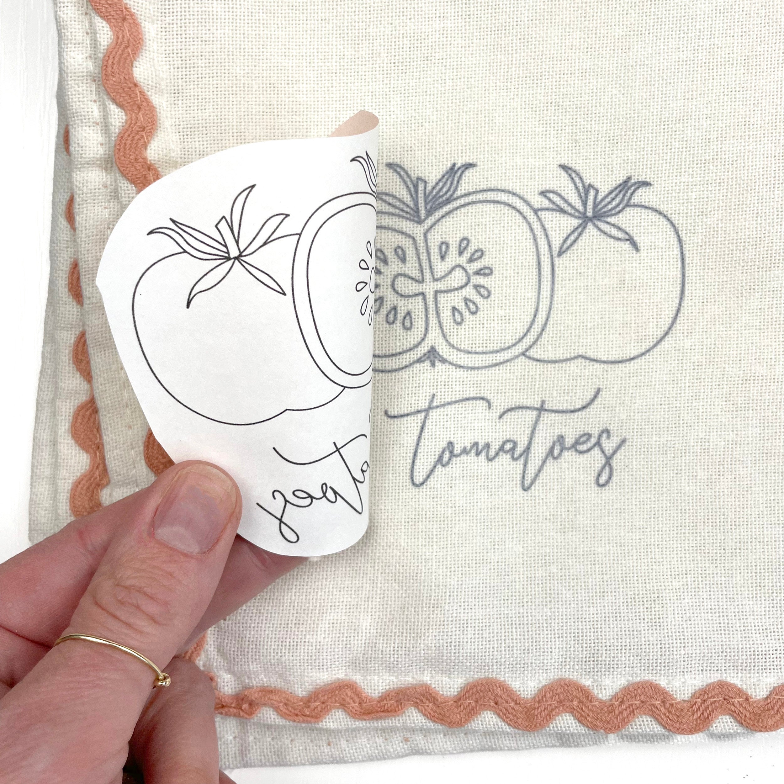 Hand holding a embroidery pattern with tomato design on a textured fabric background