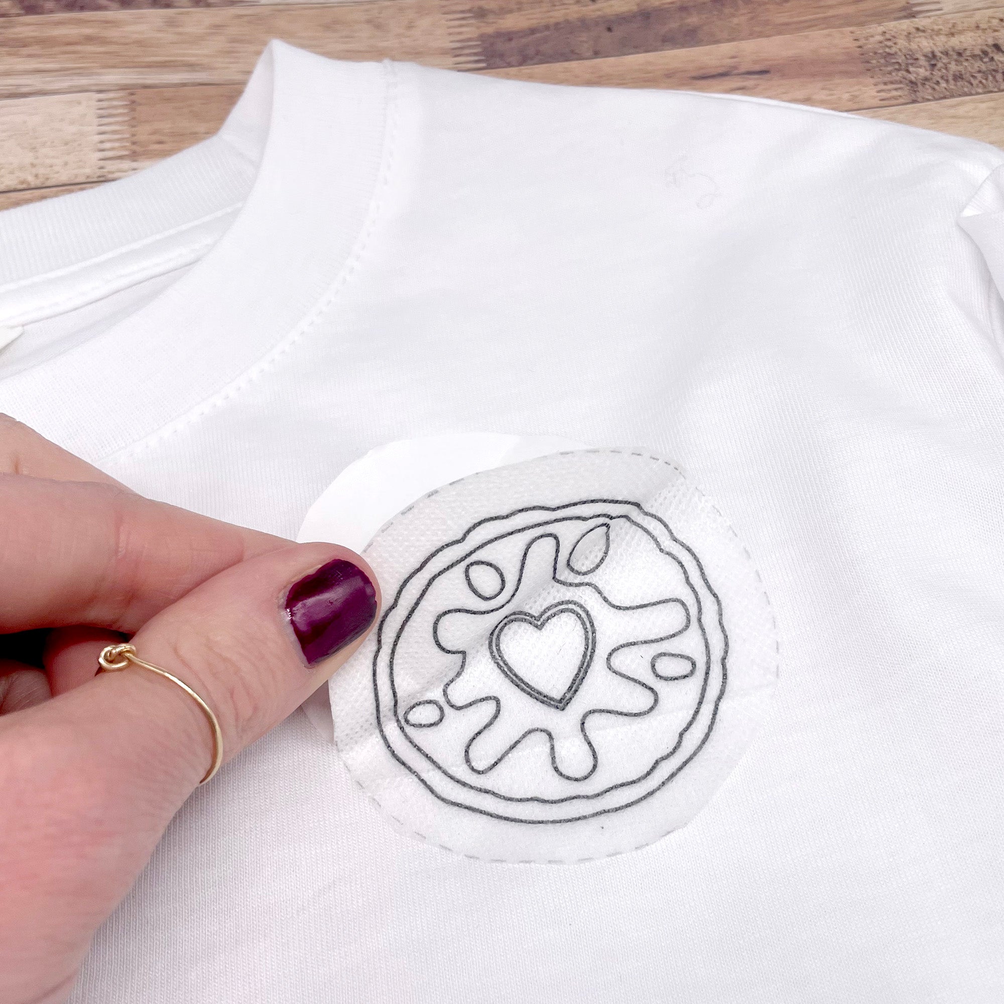 Applying a dissolving embroidery pattern of a Jammie Dodger biscuit to a white T-shirt. This stick and stitch embroidery design is perfect for modern embroidery projects and clothing embellishments.