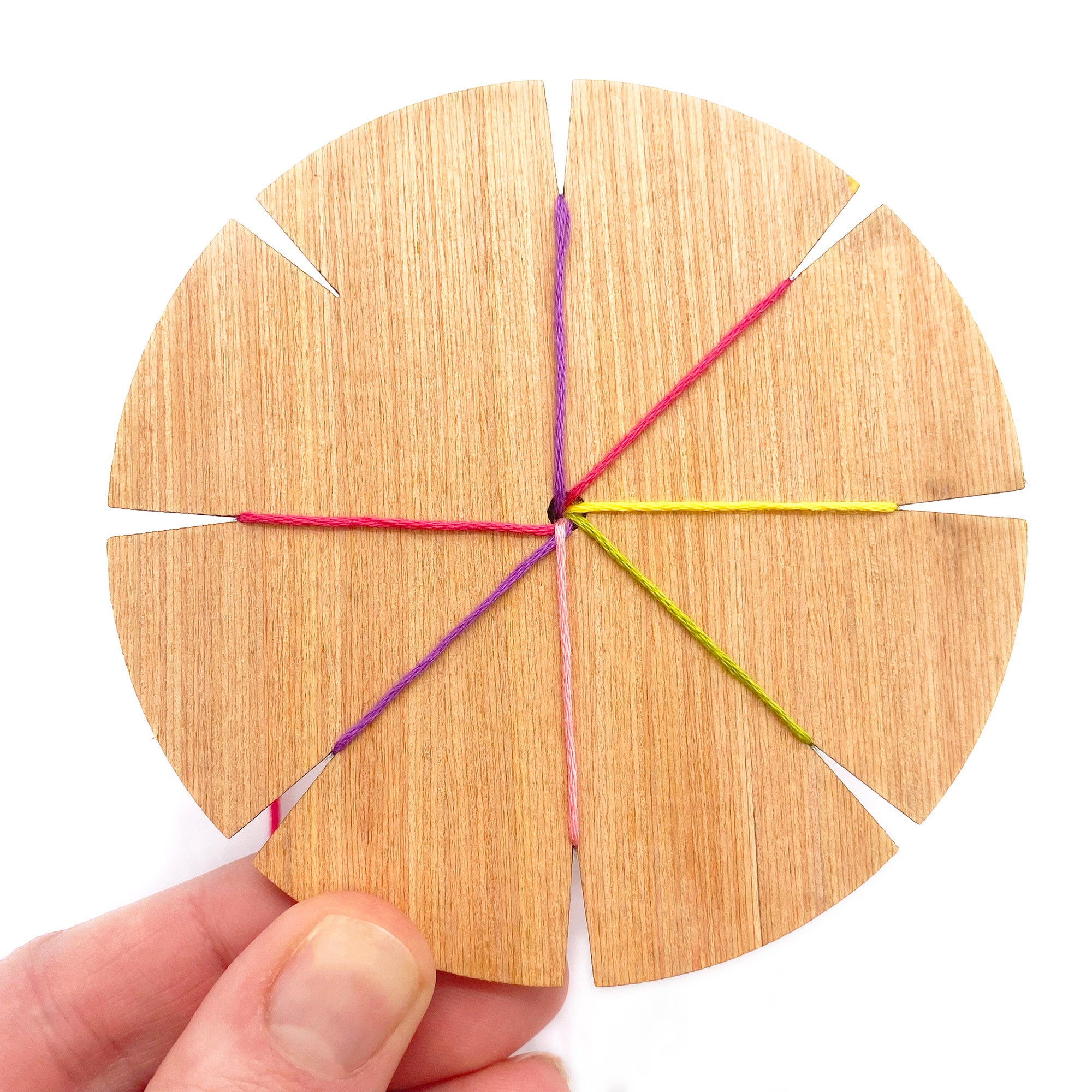 A wooden kumihimo loom held in two hands, with four strands of coloured thread in place, showing the beginning of a bracelet – part of the Lazy May woven bracelet kit.